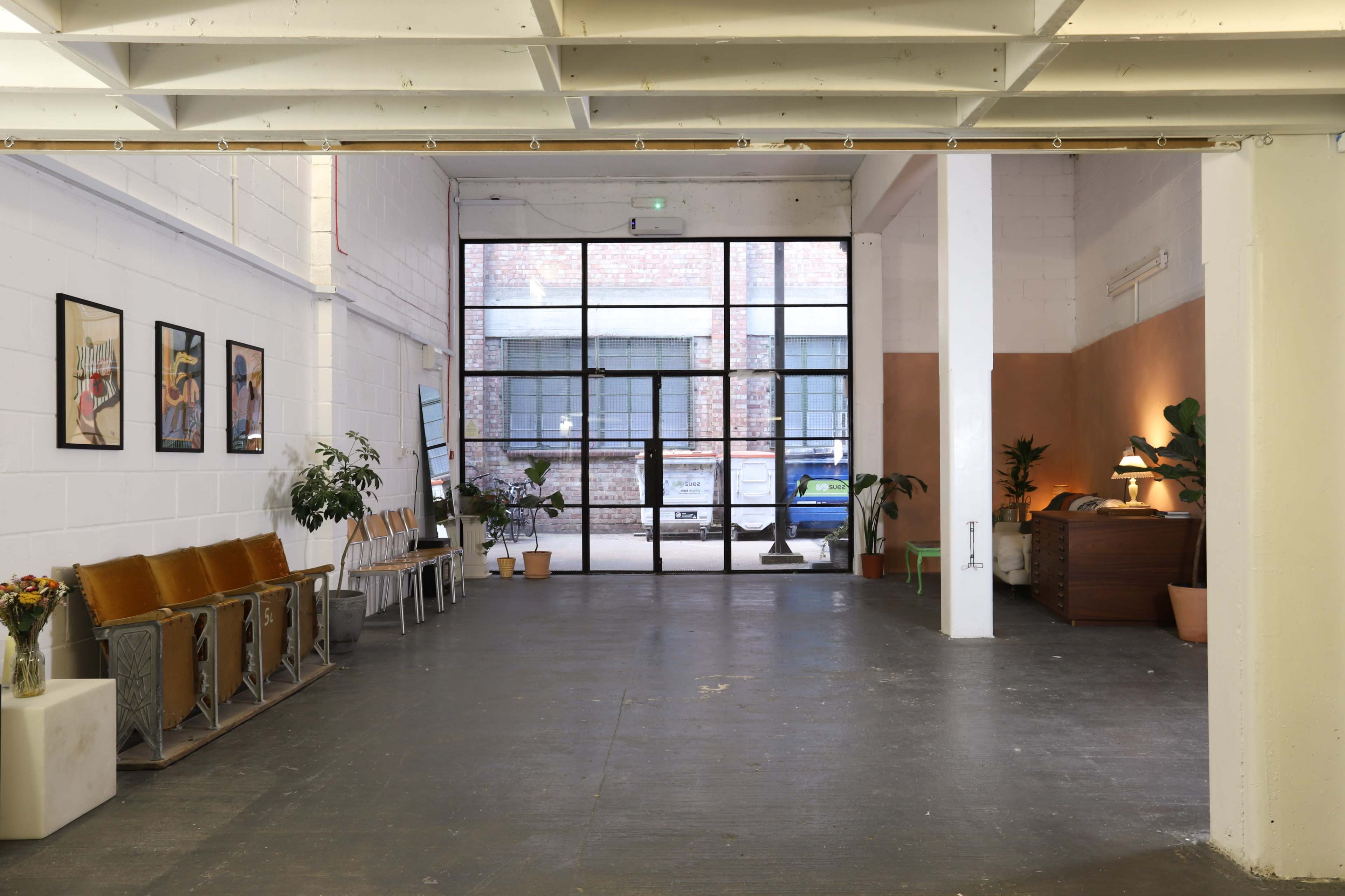 A spacious, minimalist interior with seating, plants, and large windows revealing an outdoor area.