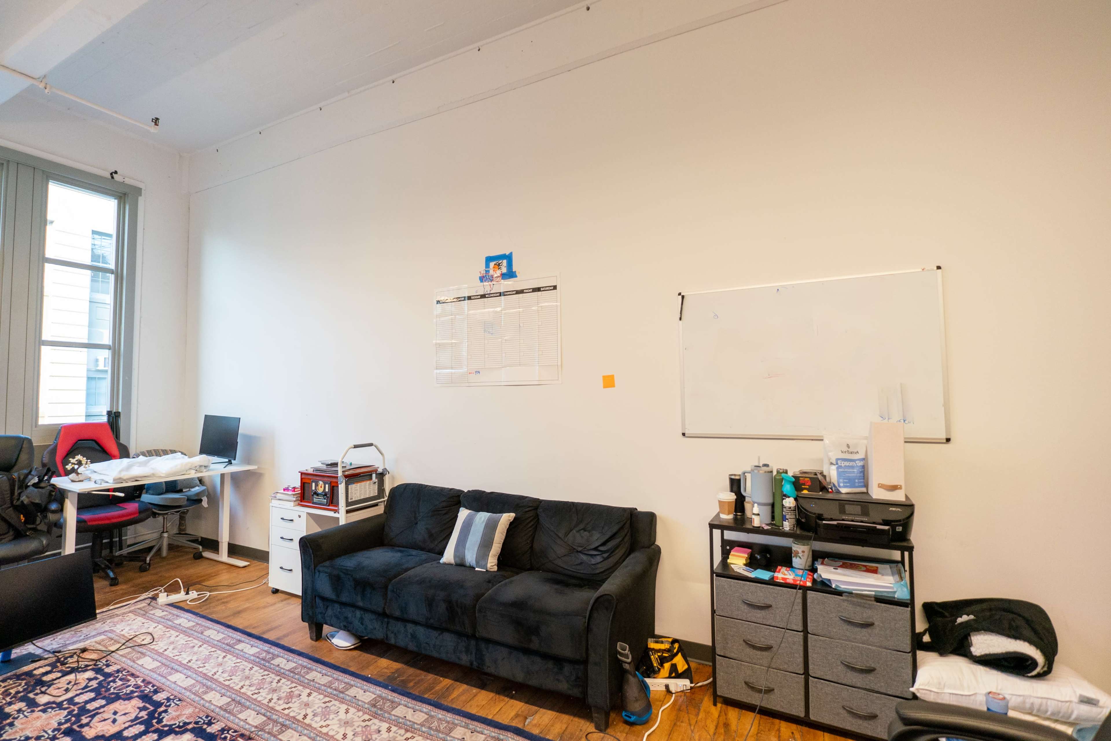 A sparse office space featuring a black couch, a coffee table, a filing cabinet, and a whiteboard on the wall.