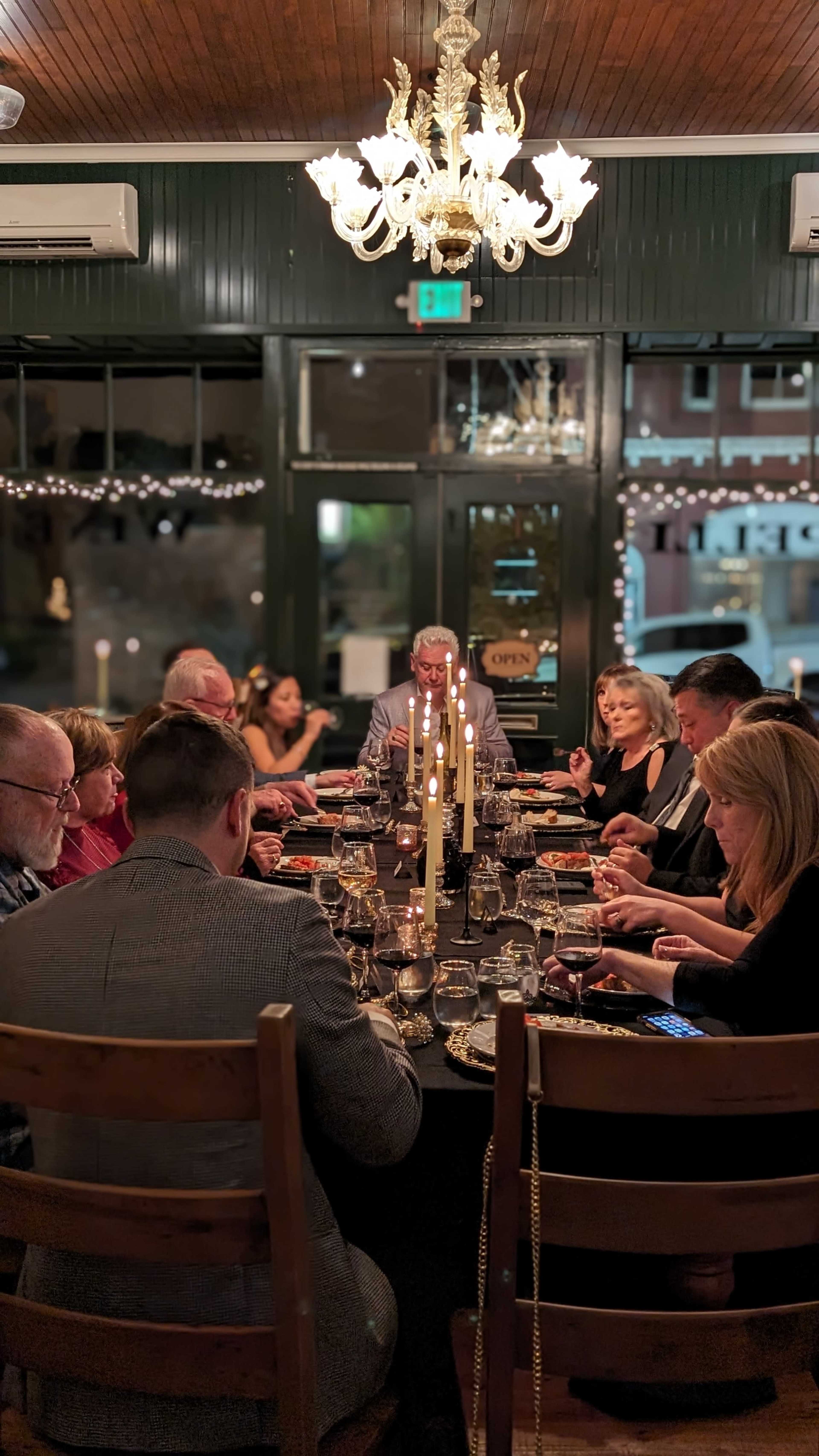 A group of people is seated around a large dining table, sharing a meal in a warmly lit restaurant adorned with decorations and candles.