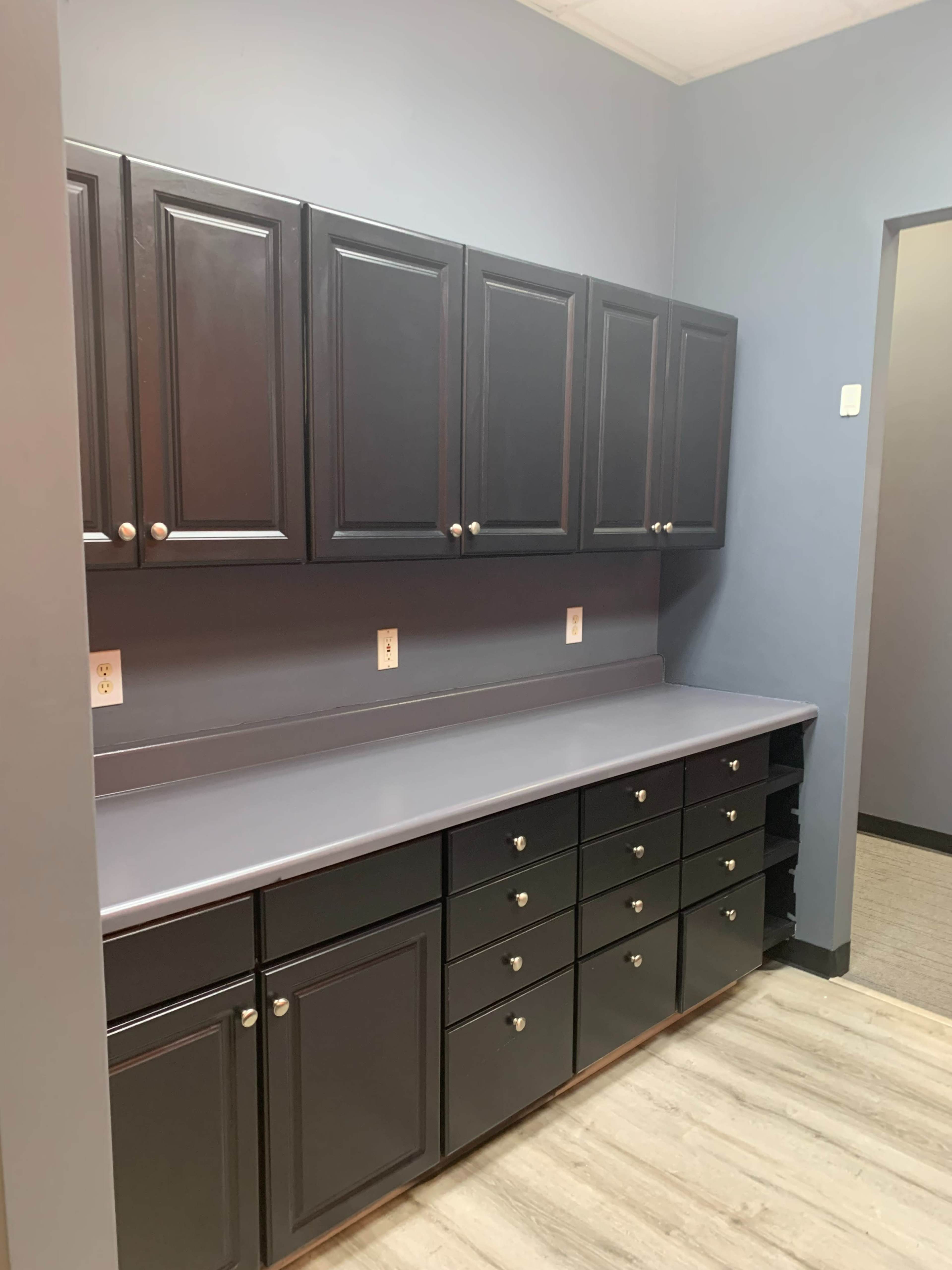 A modern utility room with dark cabinetry and a gray countertop against blue walls.