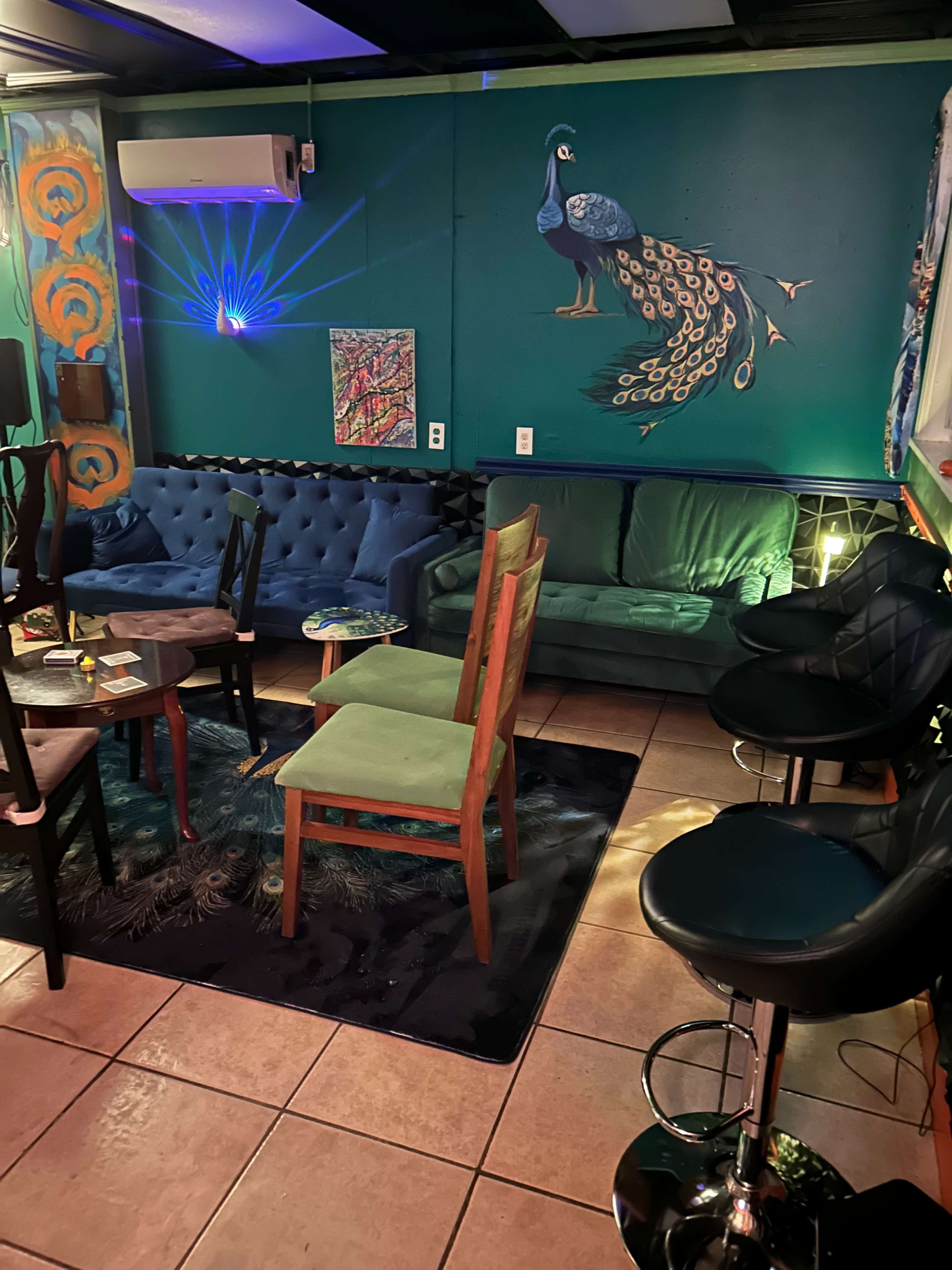The image shows a vibrant lounge area with patterned walls, two sofas, various chairs, and colorful artwork.