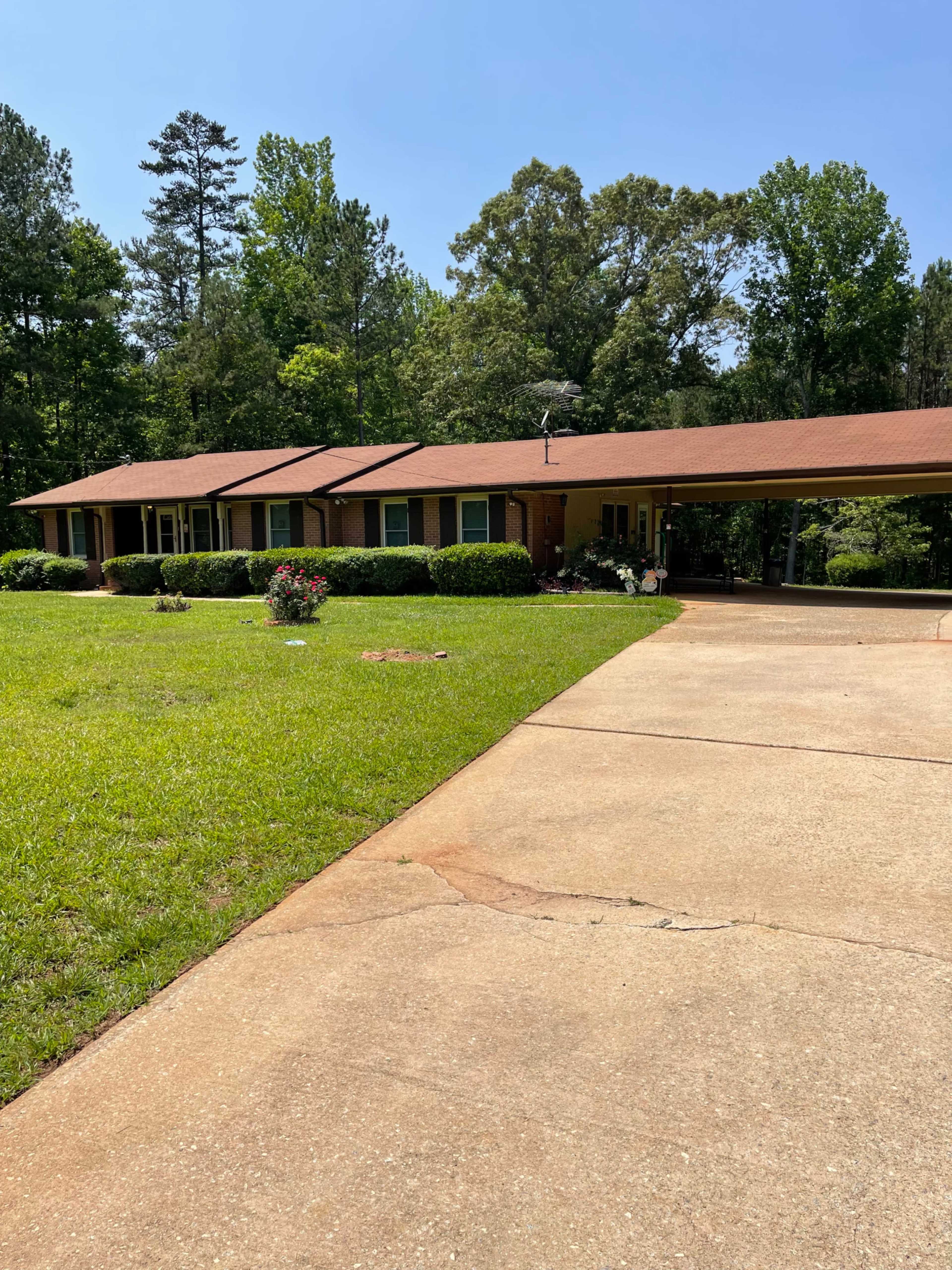 A single-story brick house with a brown roof, surrounded by a well-maintained lawn and a gravel driveway.