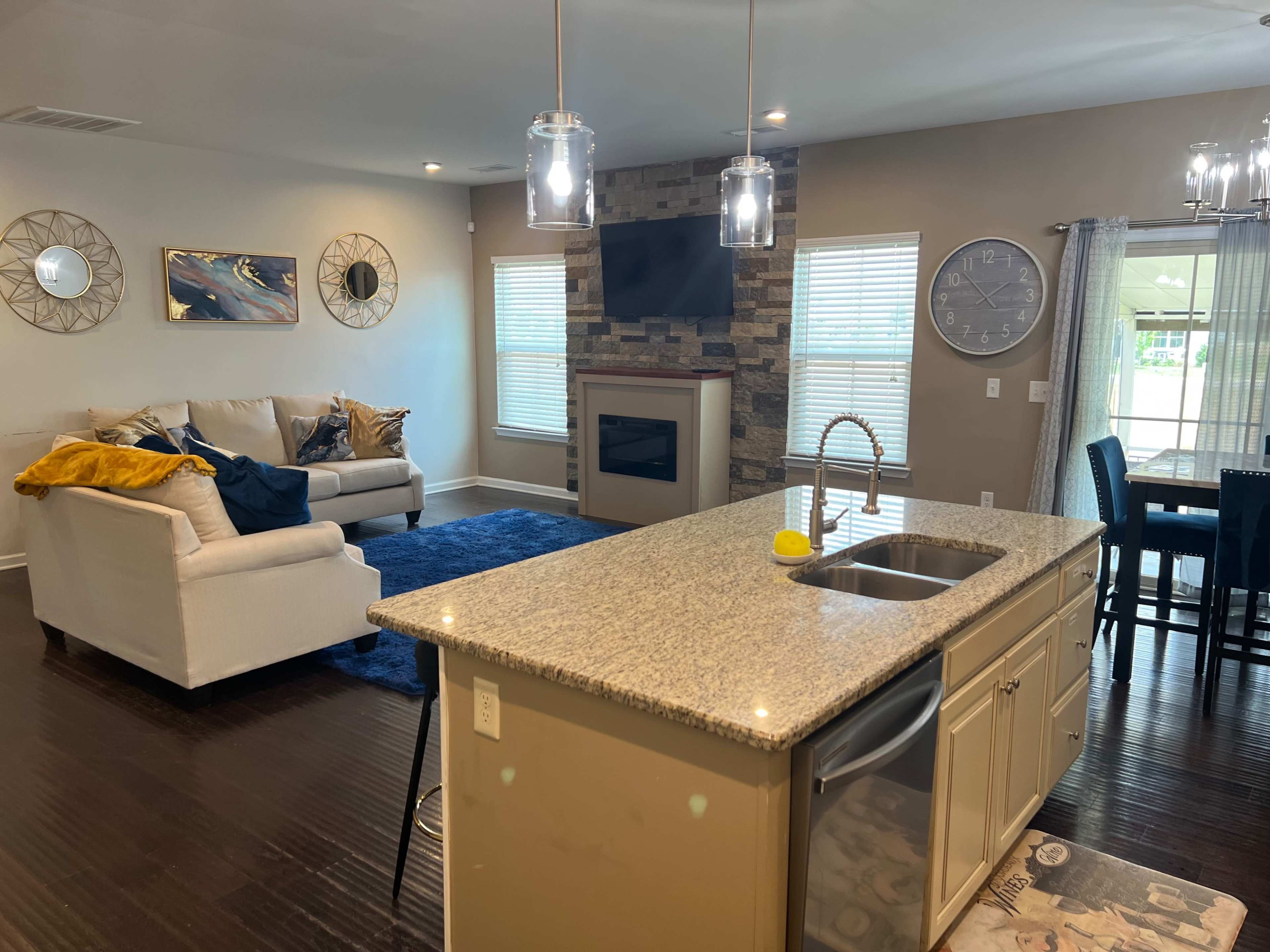 A modern living space featuring a kitchen island with a sink, a cozy seating area with a couch and a television, and a dining area with a table and chairs, all illuminated by natural light.