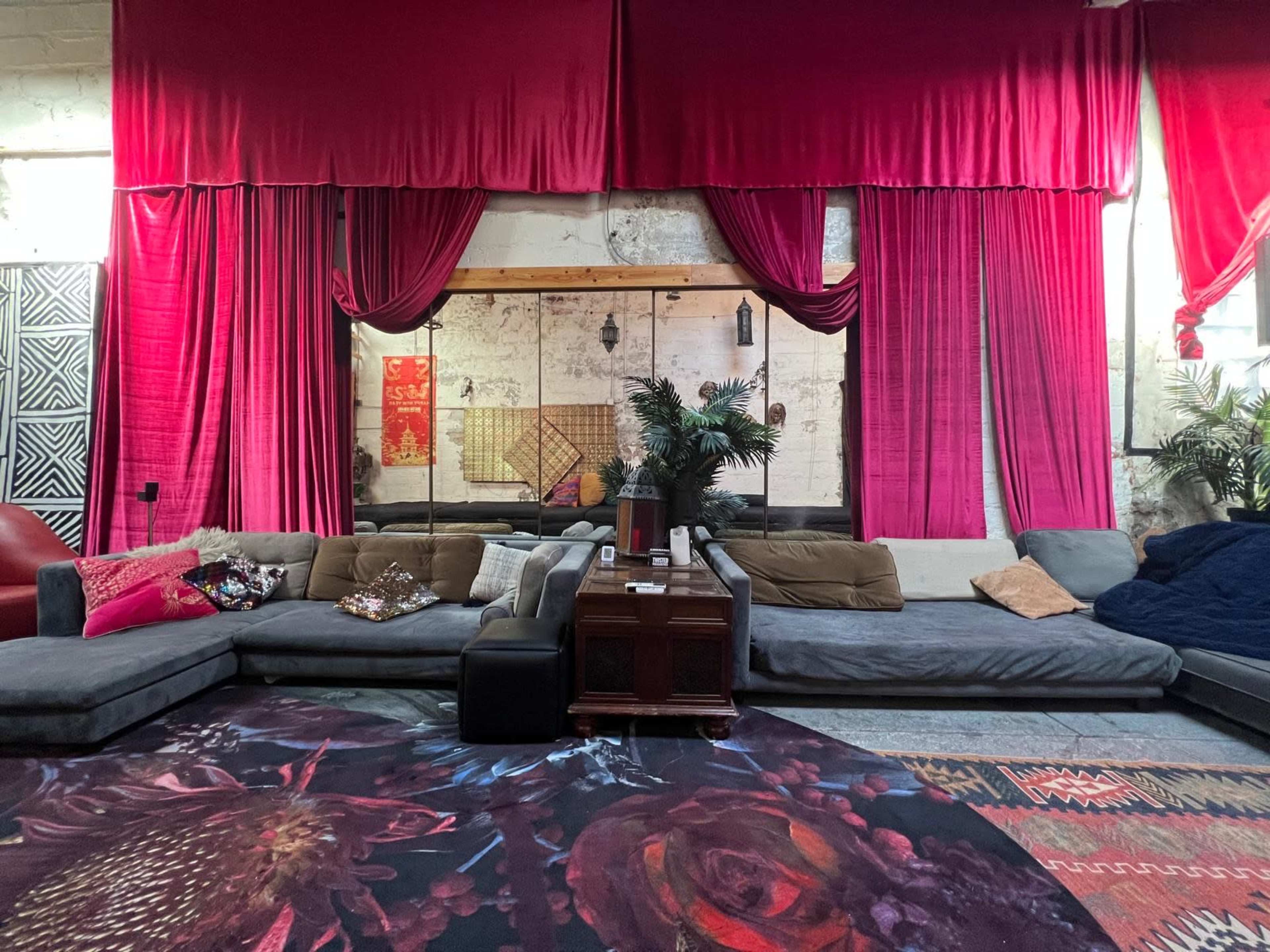 The image depicts a spacious lounge area featuring large, plush sofas, decorative curtains, and a patterned carpet.