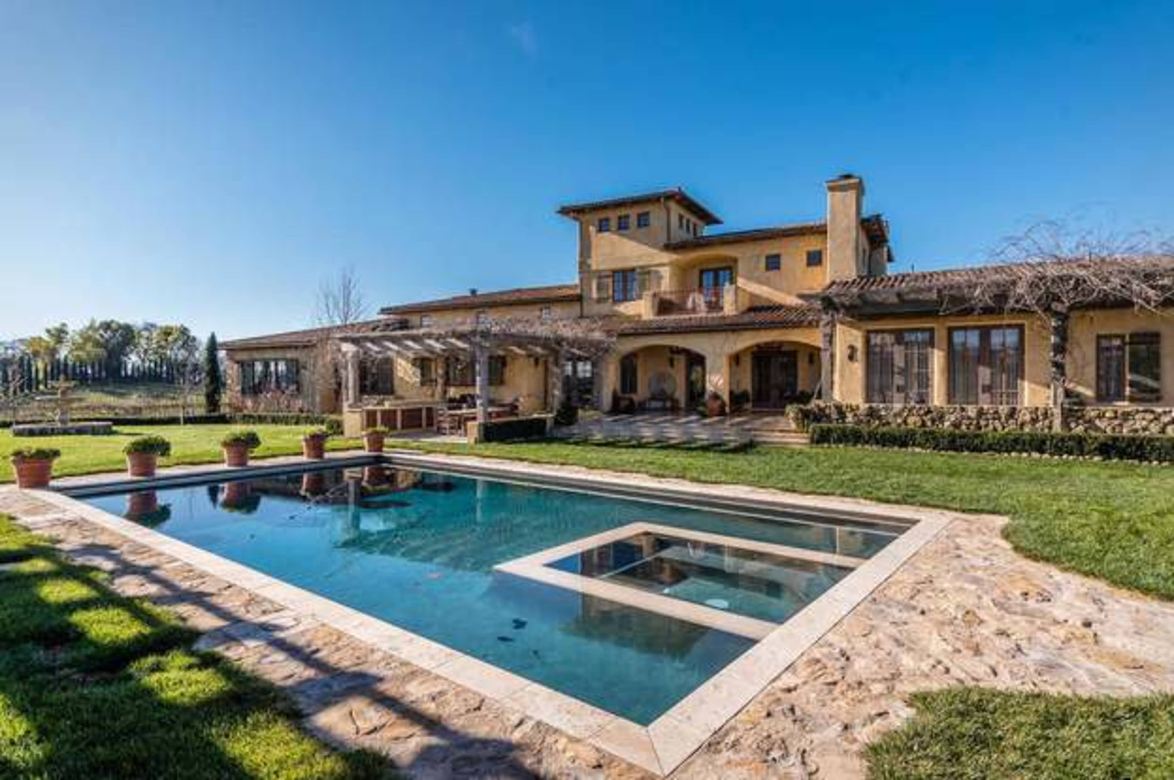 A large, two-story house with a landscaped yard features a swimming pool and an outdoor seating area.