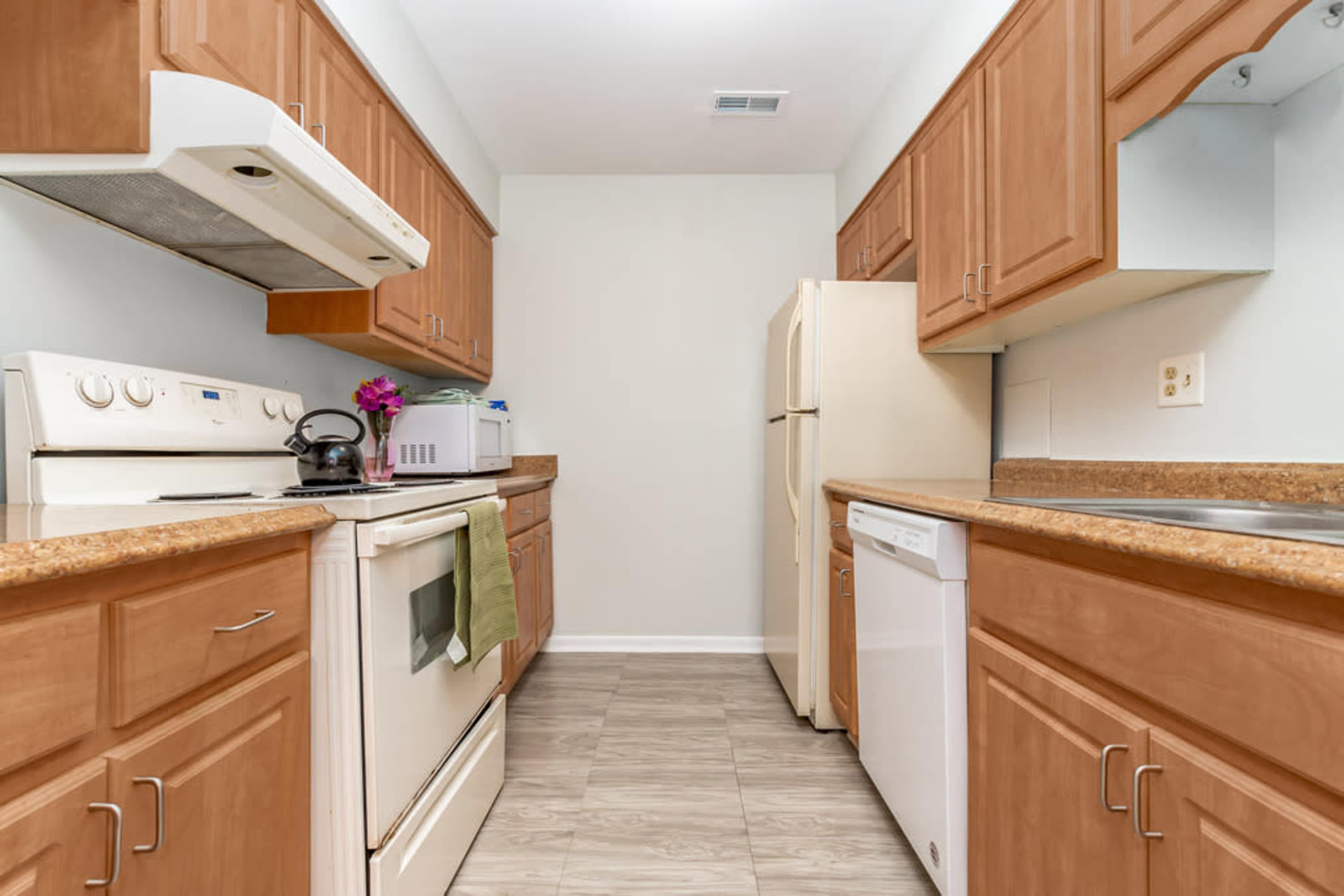 A kitchen with wooden cabinets, a white oven, and a refrigerator, featuring a counter space and a sink.