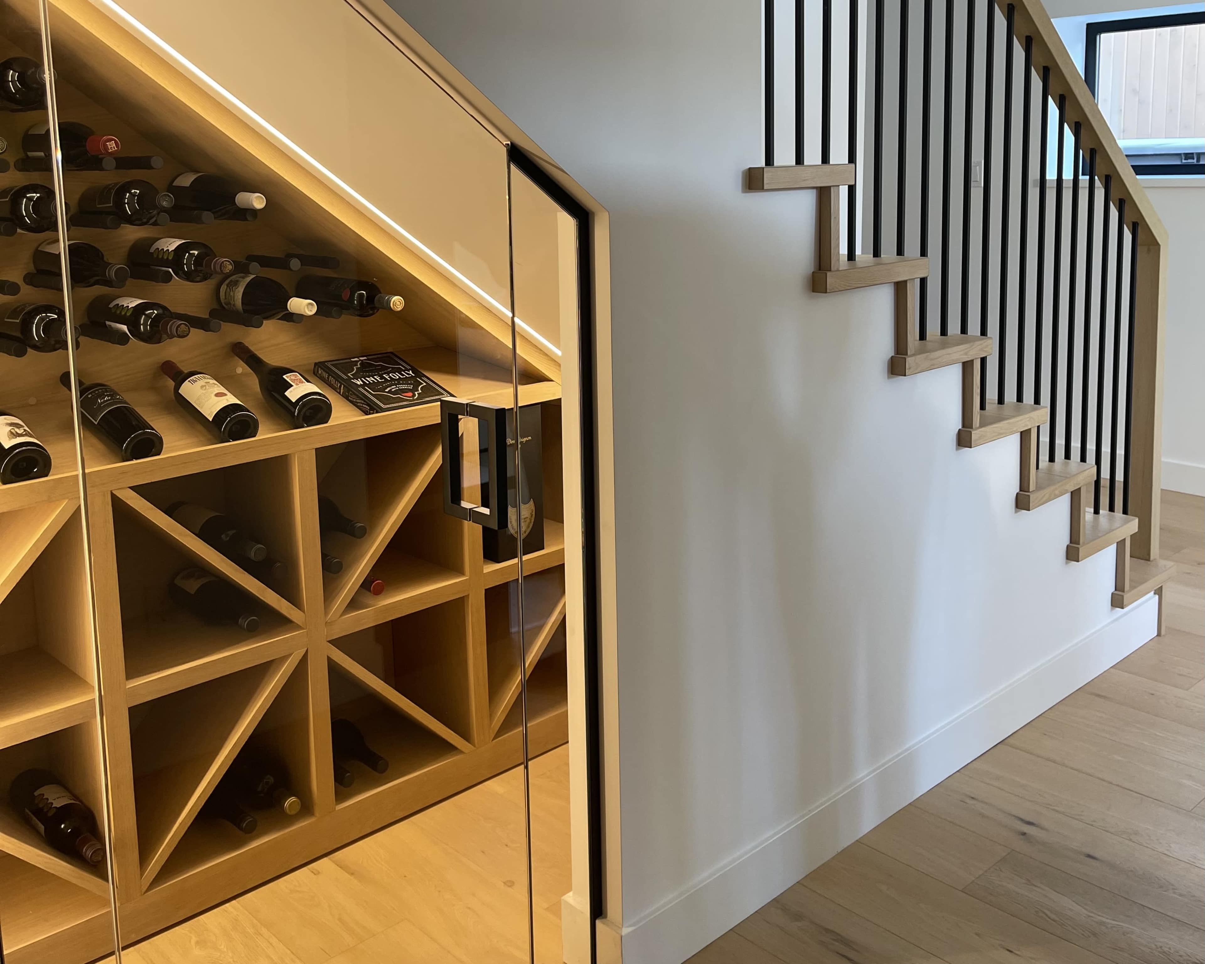 A modern staircase next to a wine storage area with wooden racks filled with bottles.