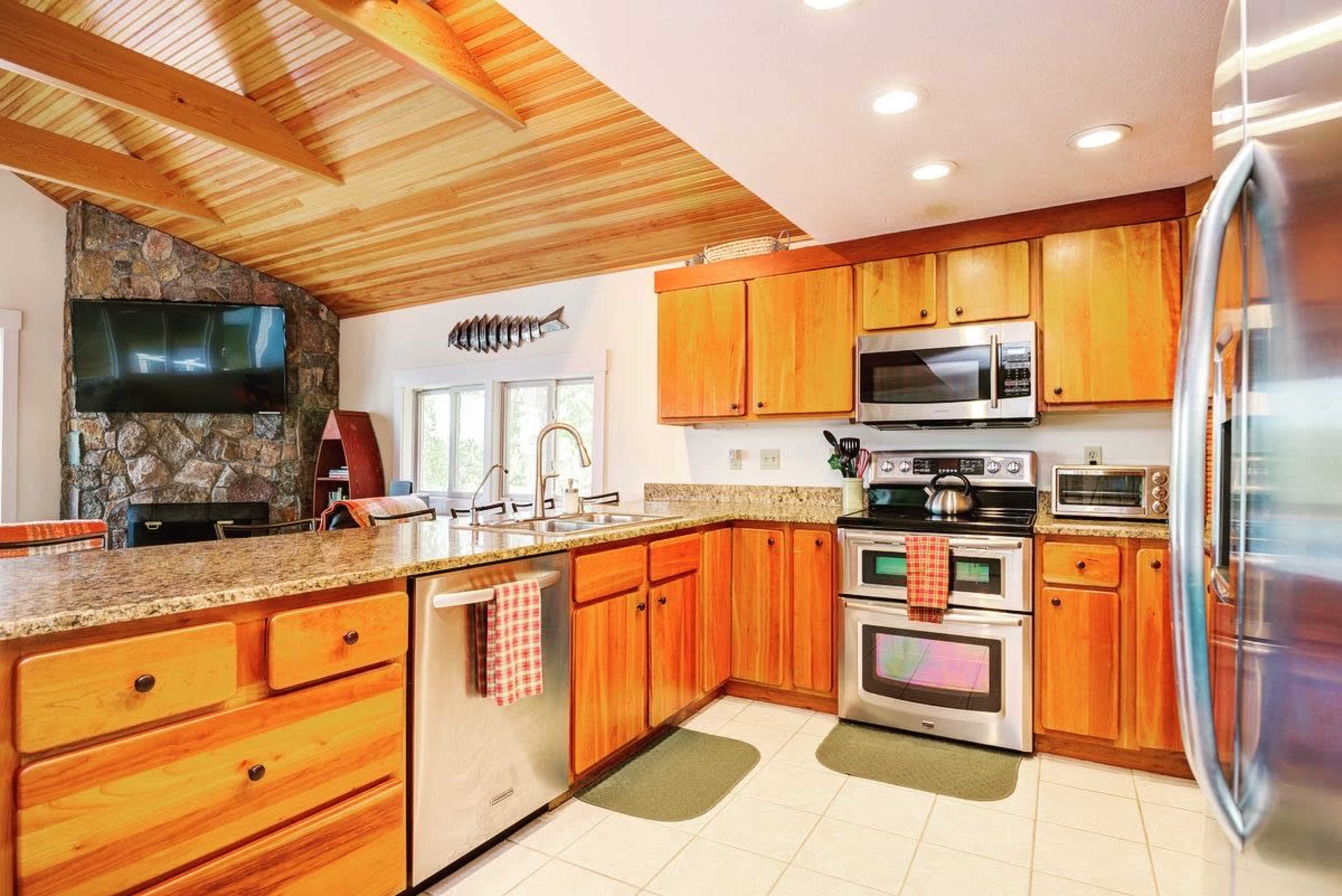 The kitchen features wooden cabinets, stainless steel appliances, and a granite countertop beneath a vaulted ceiling with exposed beams.