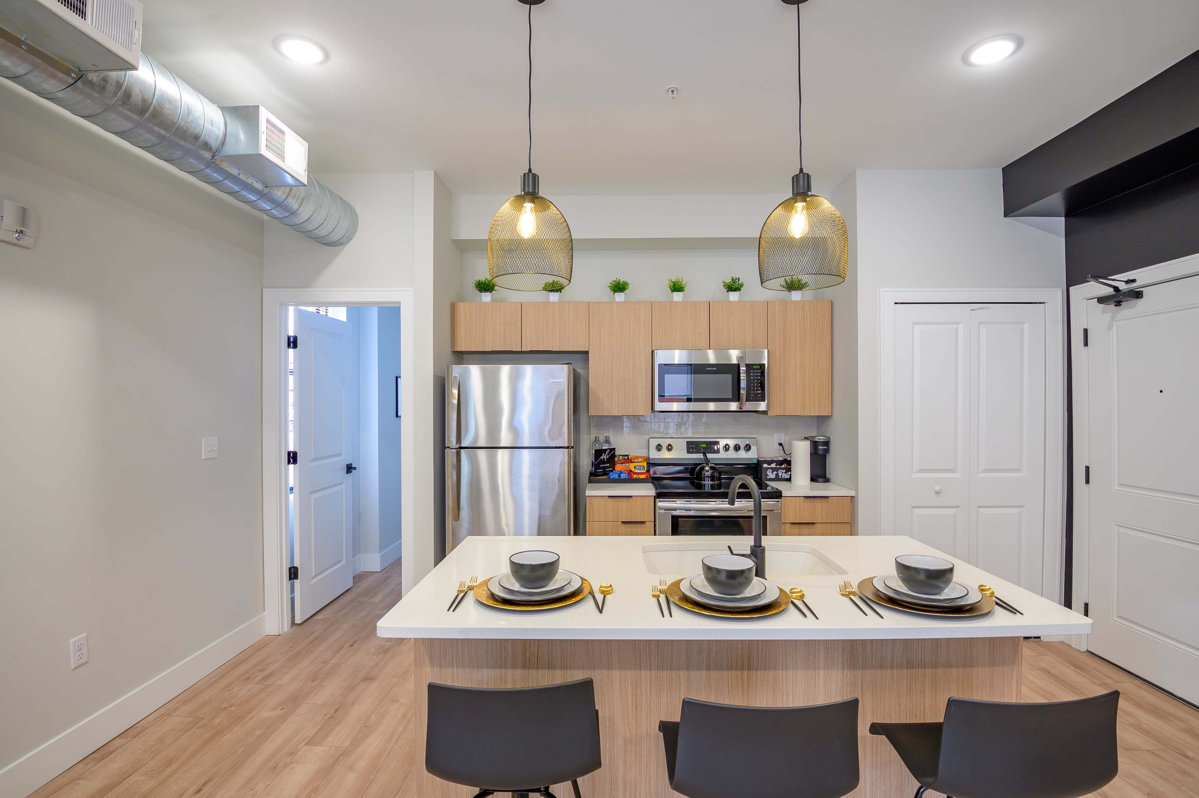 A modern kitchen with a dining area featuring a central island, stainless steel appliances, and three place settings.
