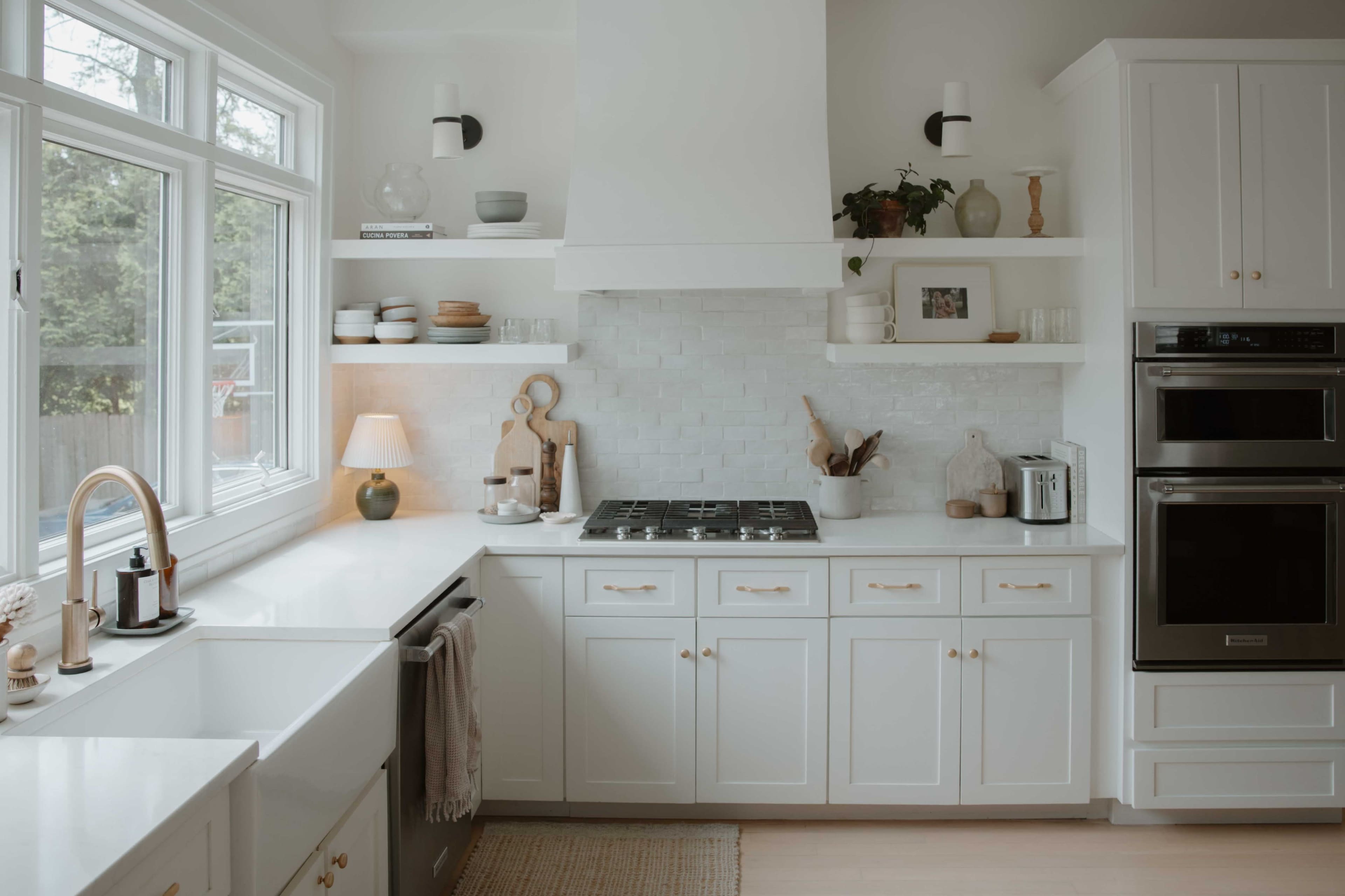 The image shows a modern kitchen with white cabinetry, a gas stove, and open shelves displaying various kitchenware and decor.