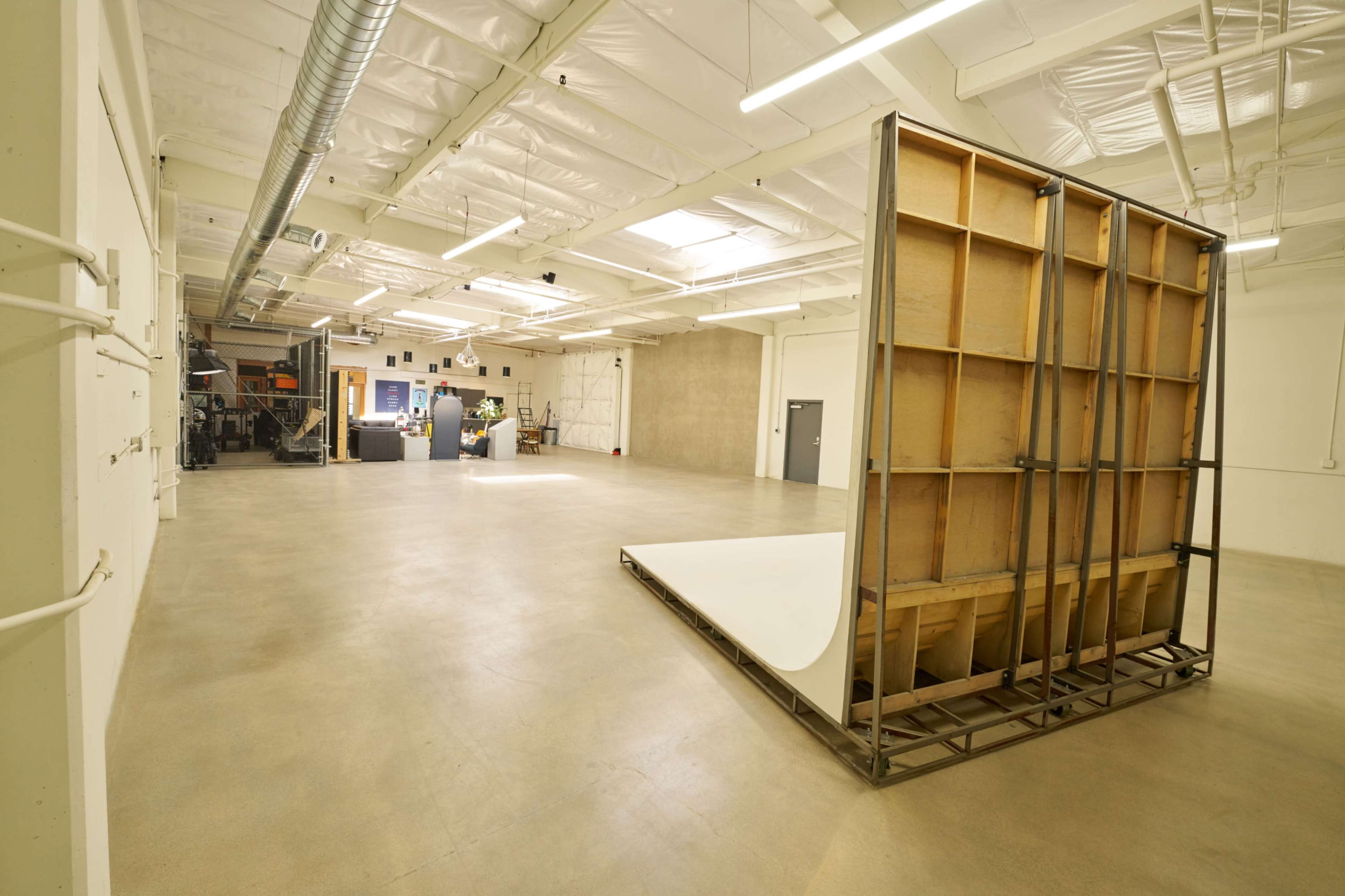 The image shows a spacious, empty studio with a large backdrop support structure and a white seamless floor section.
