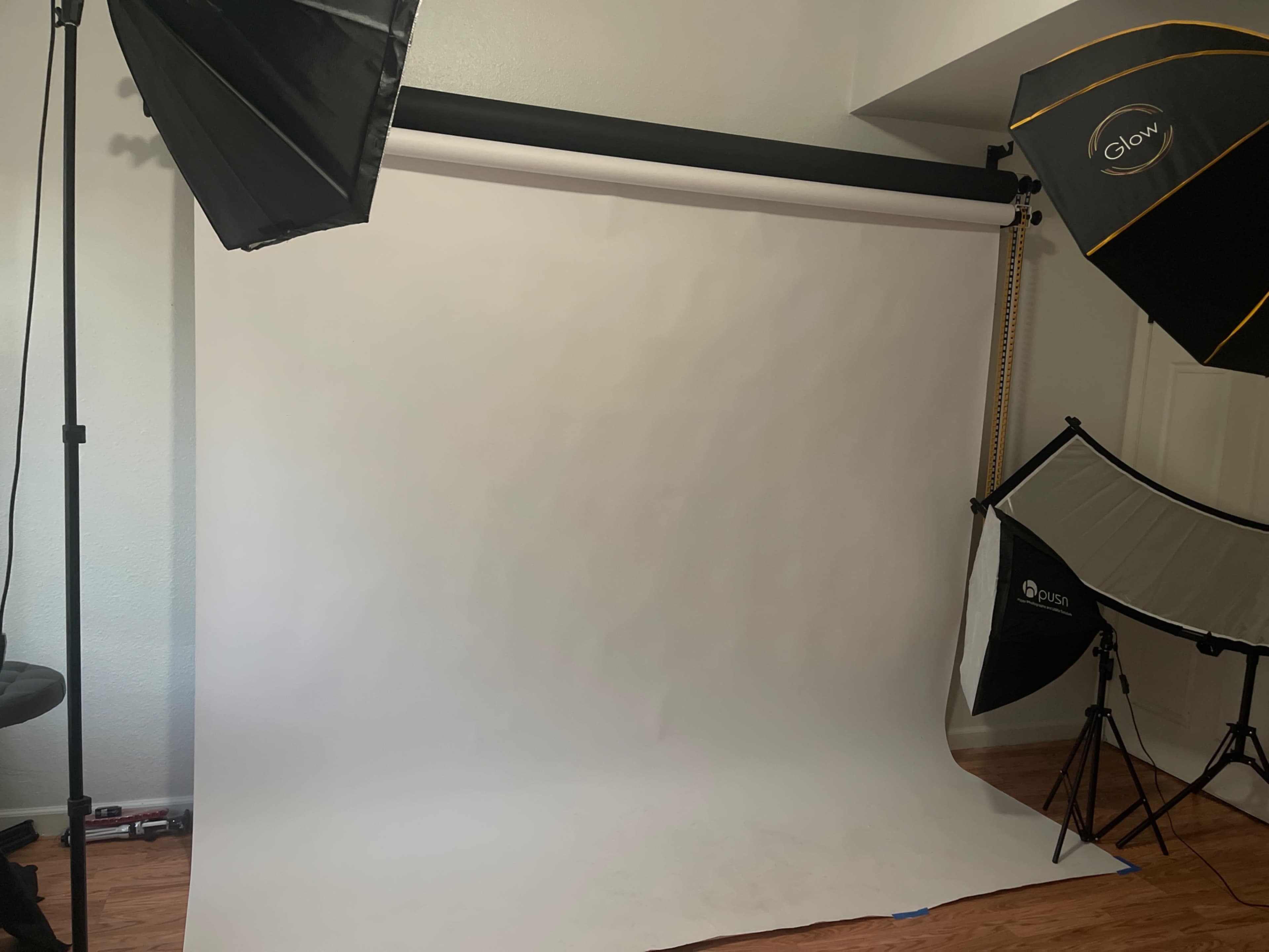 A photography studio setup with a white backdrop and various lighting equipment arranged around it.