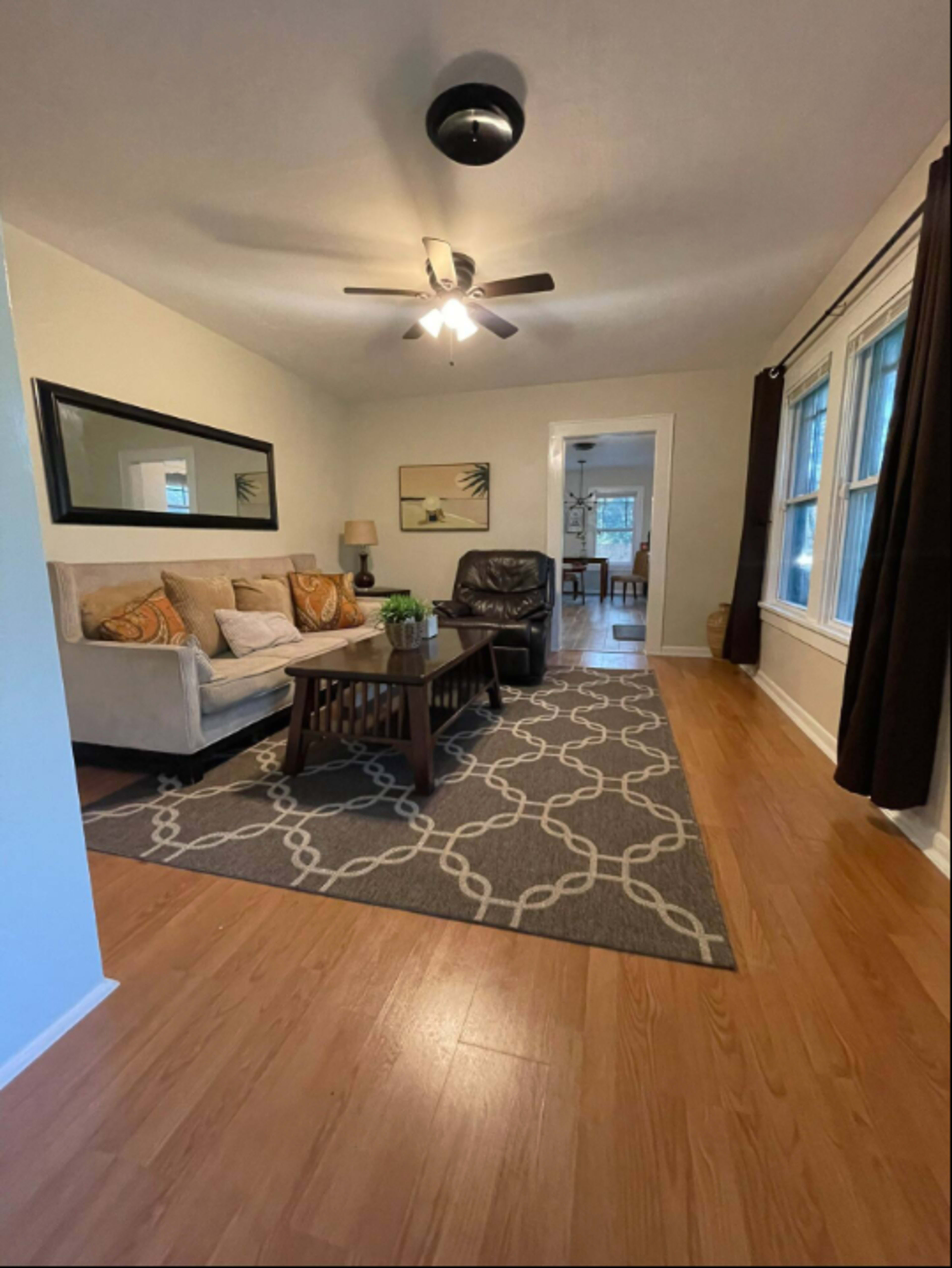 A living room with a sofa and armchair, a coffee table, and a patterned area rug on a wooden floor.