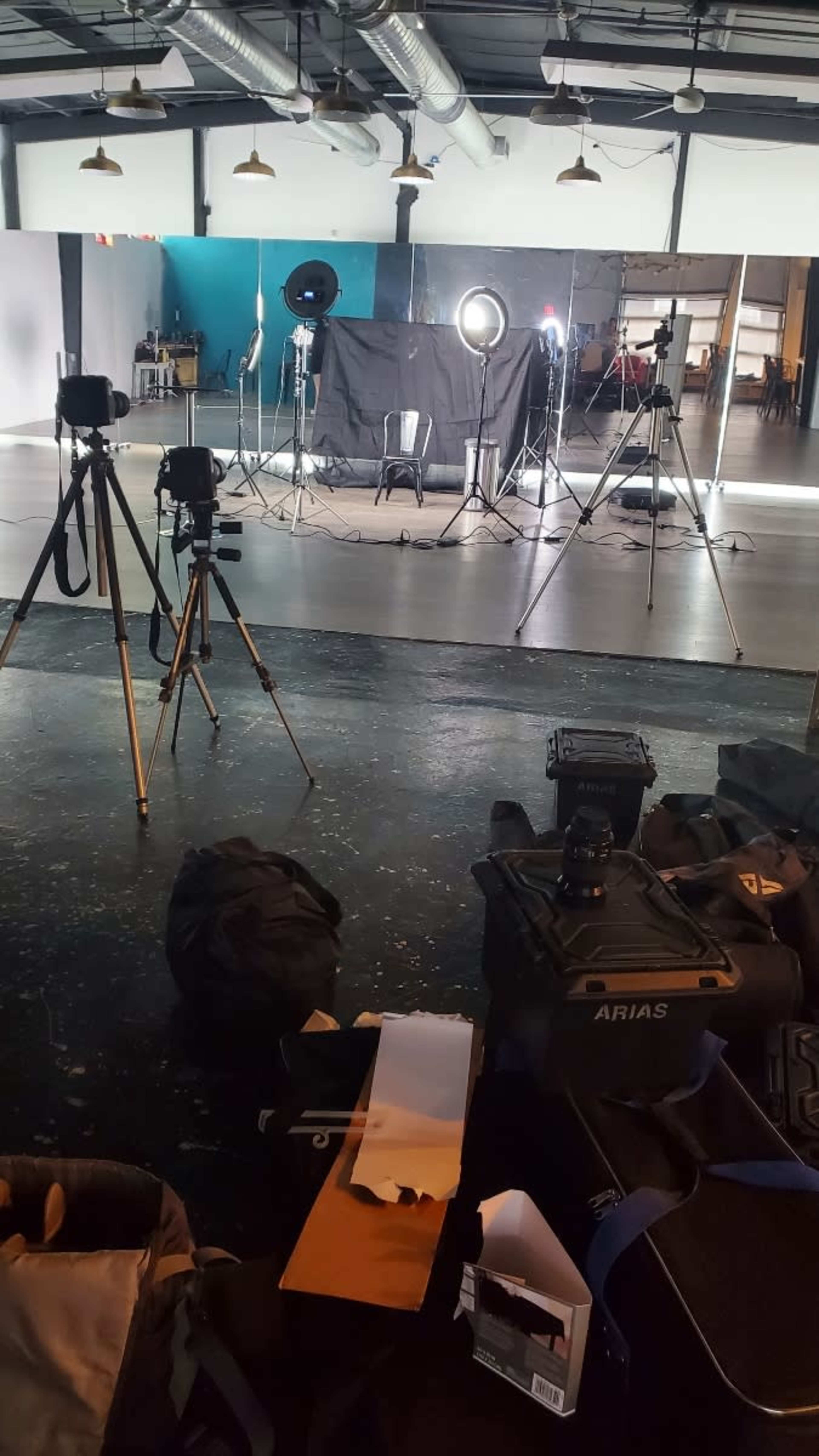 A photography studio is set up with multiple cameras, lighting equipment, and a chair in front of a backdrop.