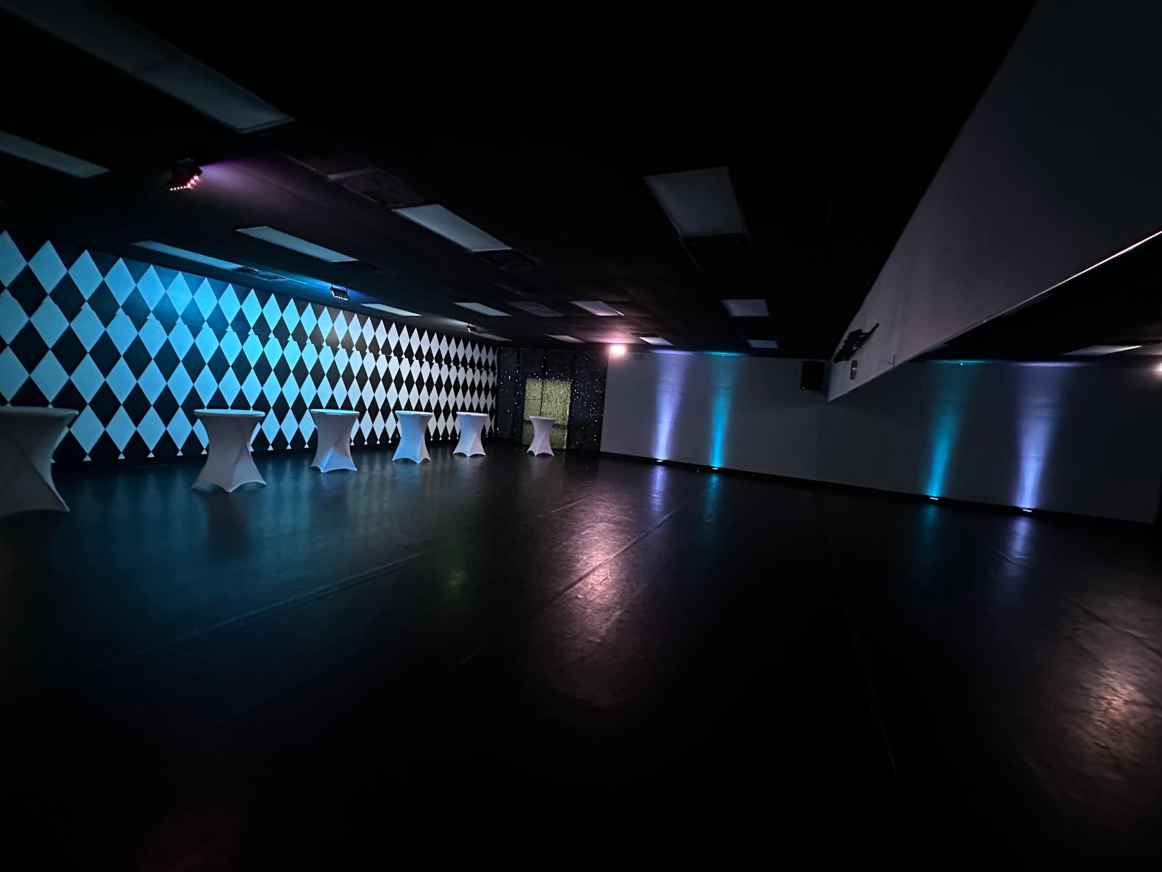 An empty event space with a checkered wall and illuminated tables.