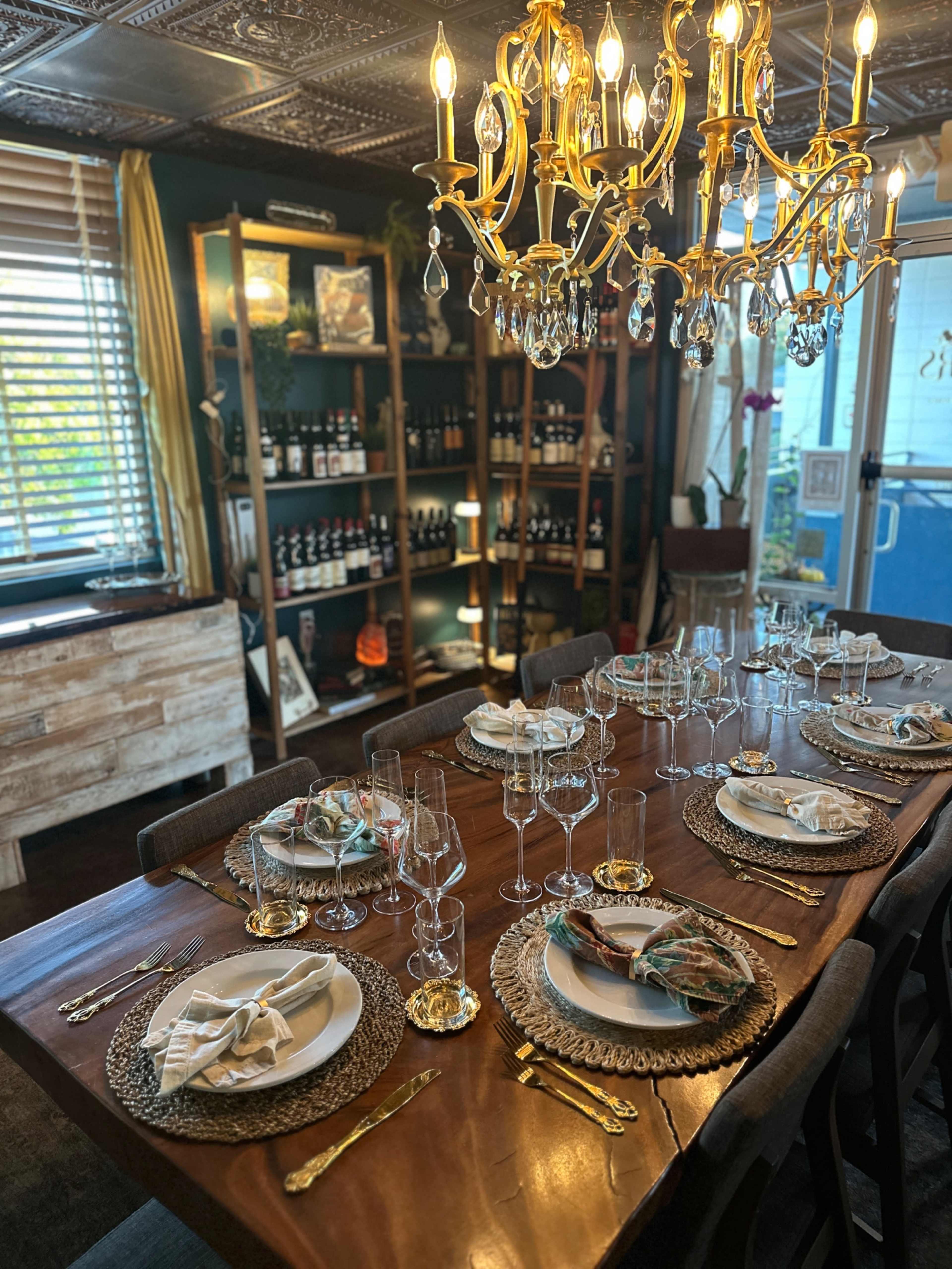 The image shows a dining table set with plates, glasses, and decorative napkins, surrounded by a well-organized display of wine bottles on shelves in a warmly-lit room.