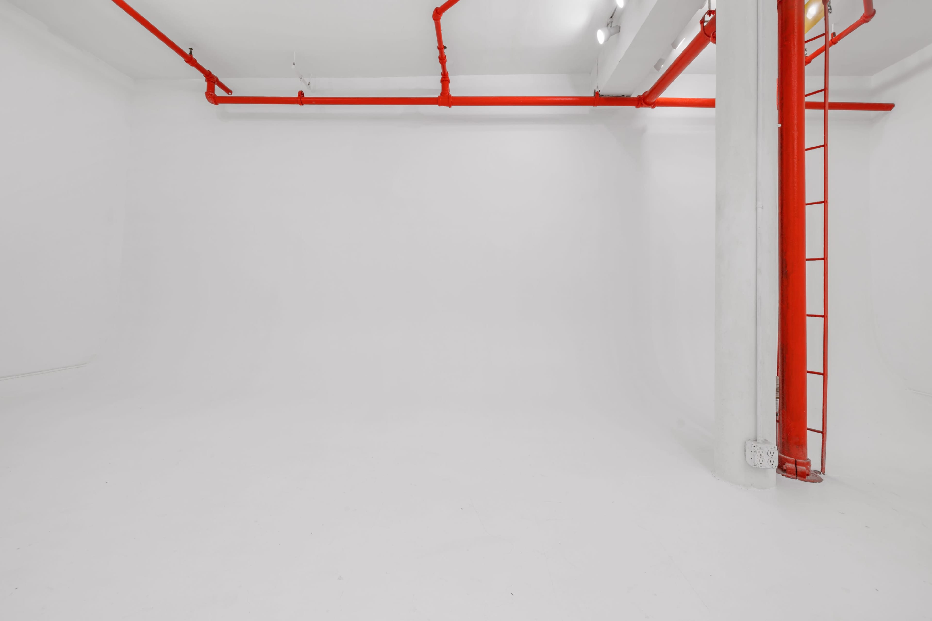 A minimalistic white room with red piping and a red ladder against one wall.