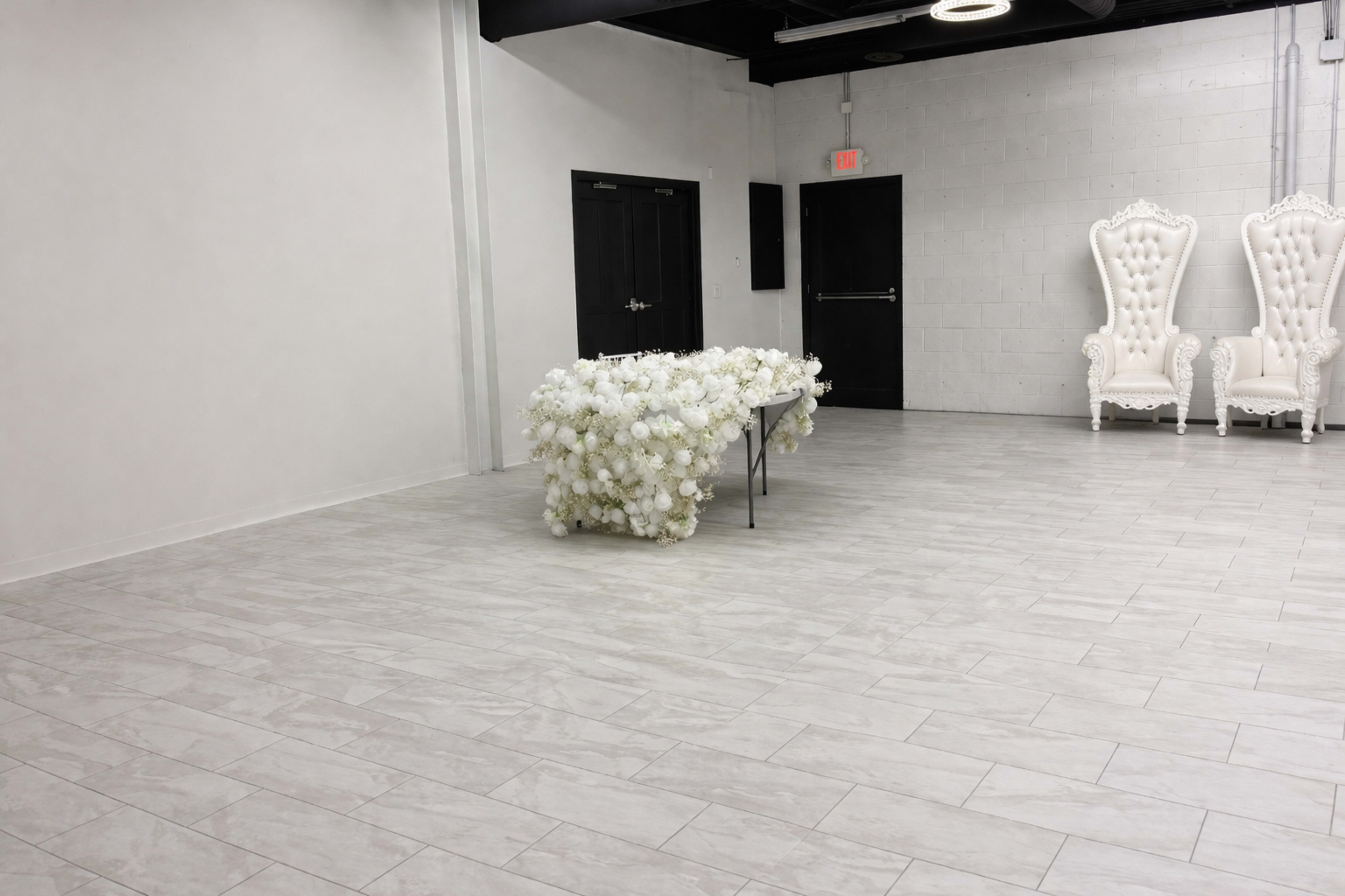 A spacious, minimalistic room features a table adorned with white flowers and two large, ornate white chairs in the background.