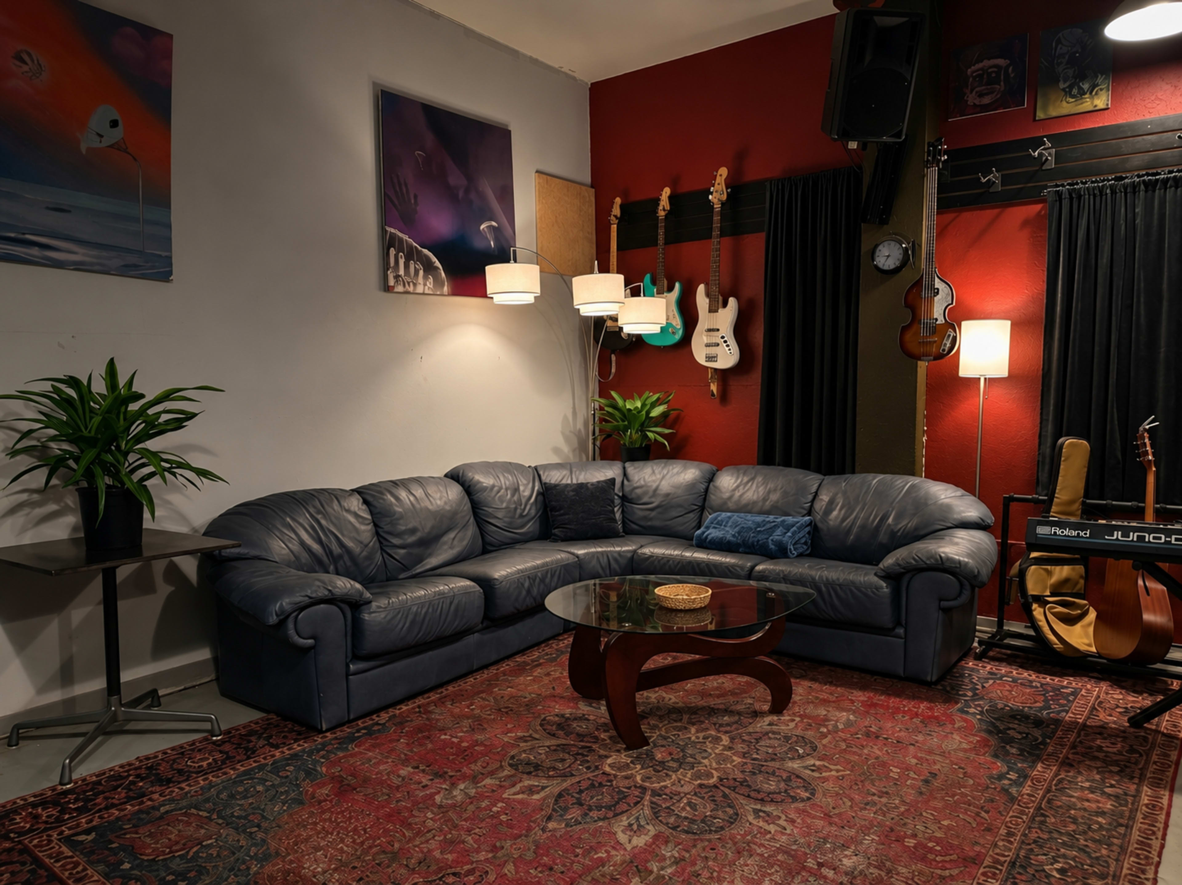 The image shows a cozy living room with a blue leather sectional sofa, a glass coffee table, and musical instruments hanging on the wall.