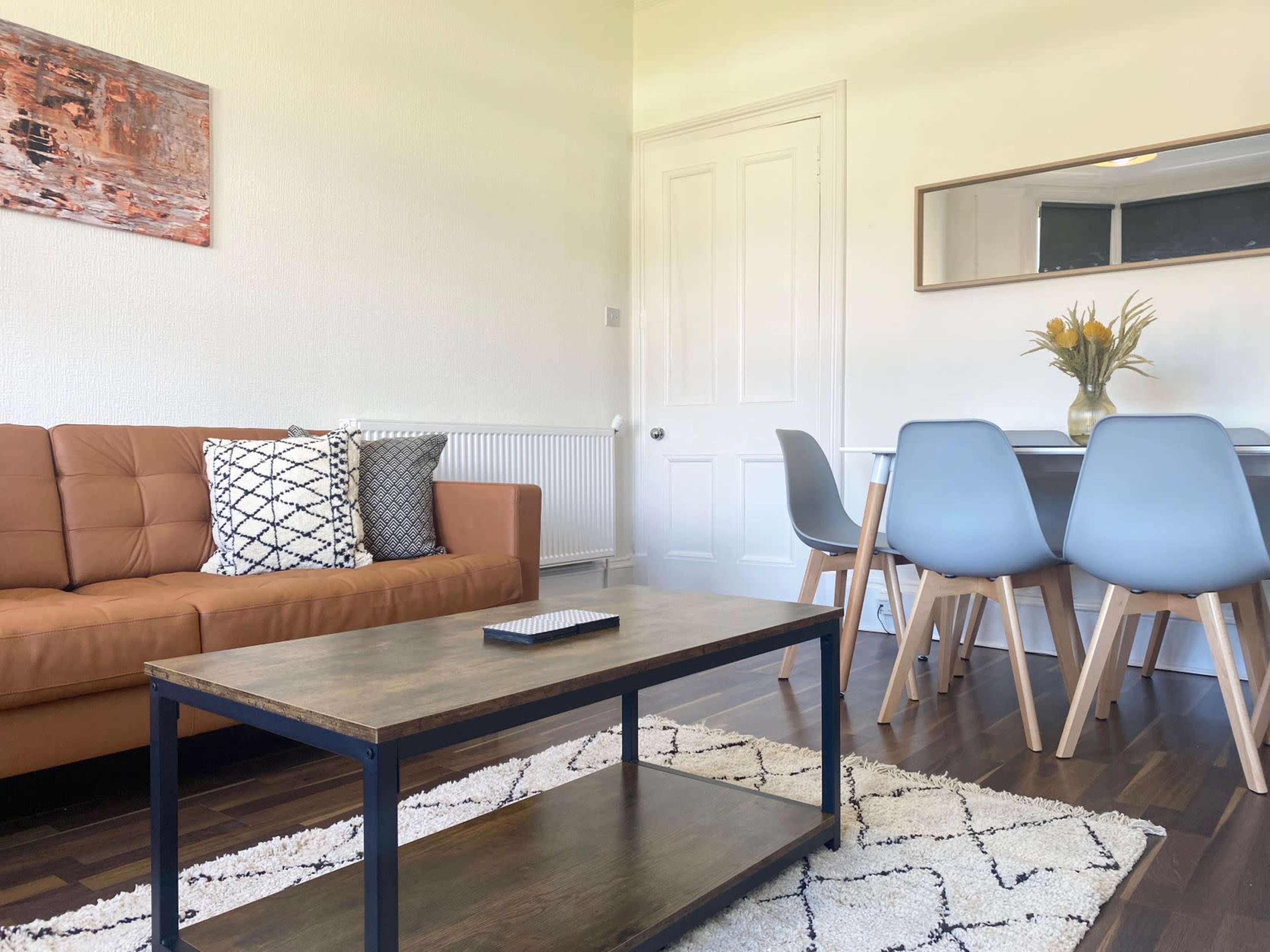 A living room features a brown sofa, a wooden coffee table, and a dining area with light blue chairs and a table.