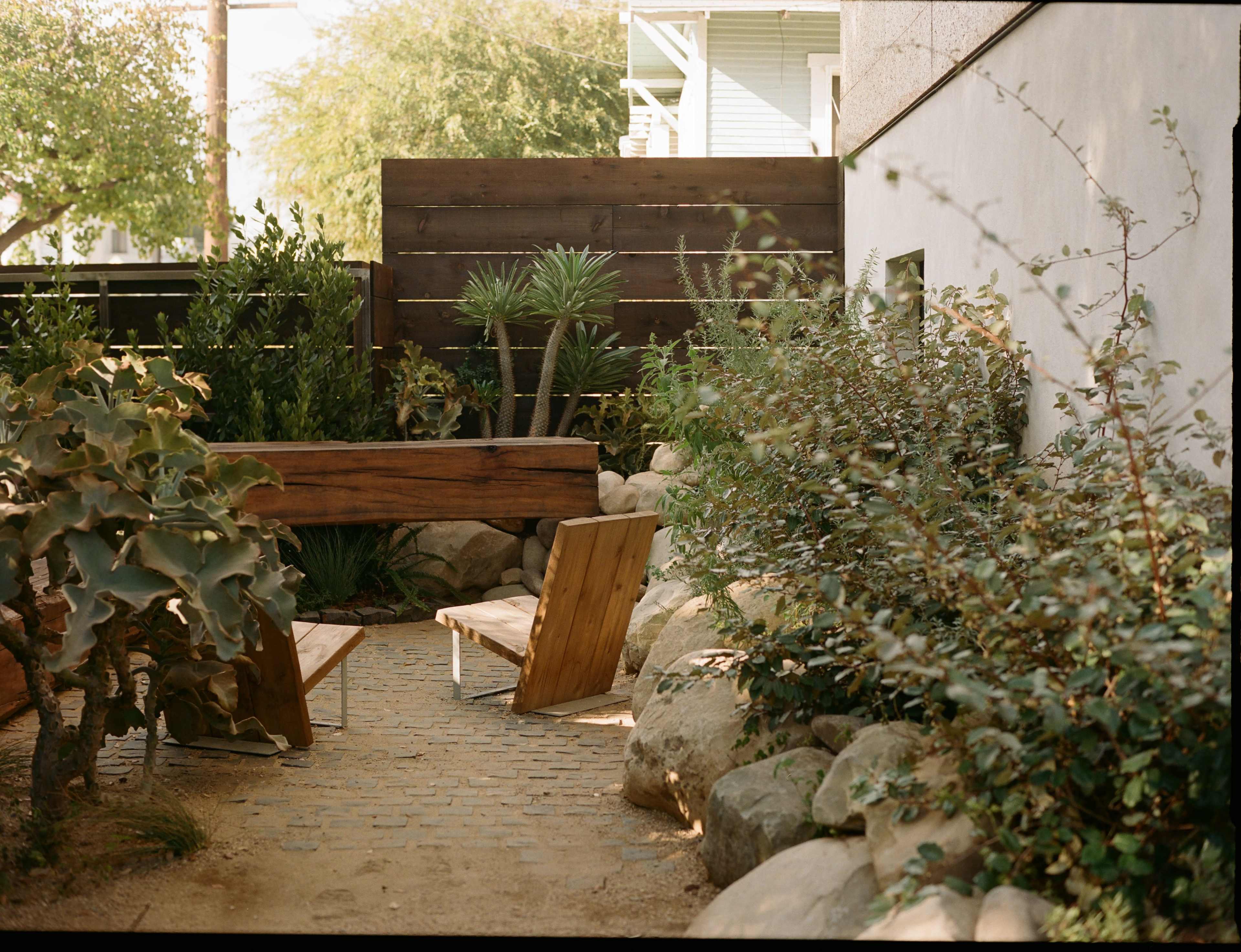 A wooden bench and chair are situated among lush greenery and rocks in a small garden area.