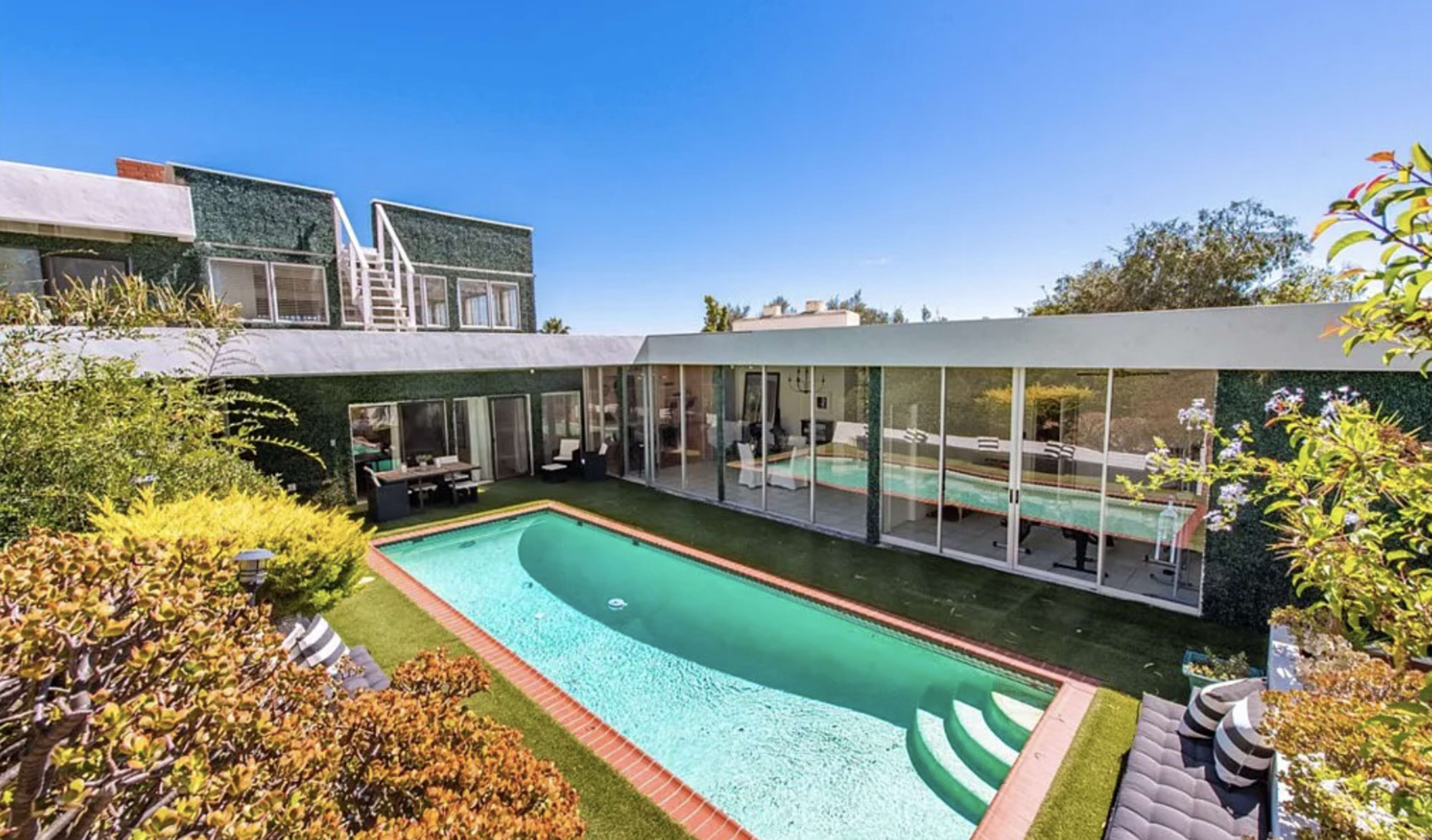 A modern home with a glass facade and a rectangular swimming pool surrounded by landscaped greenery.