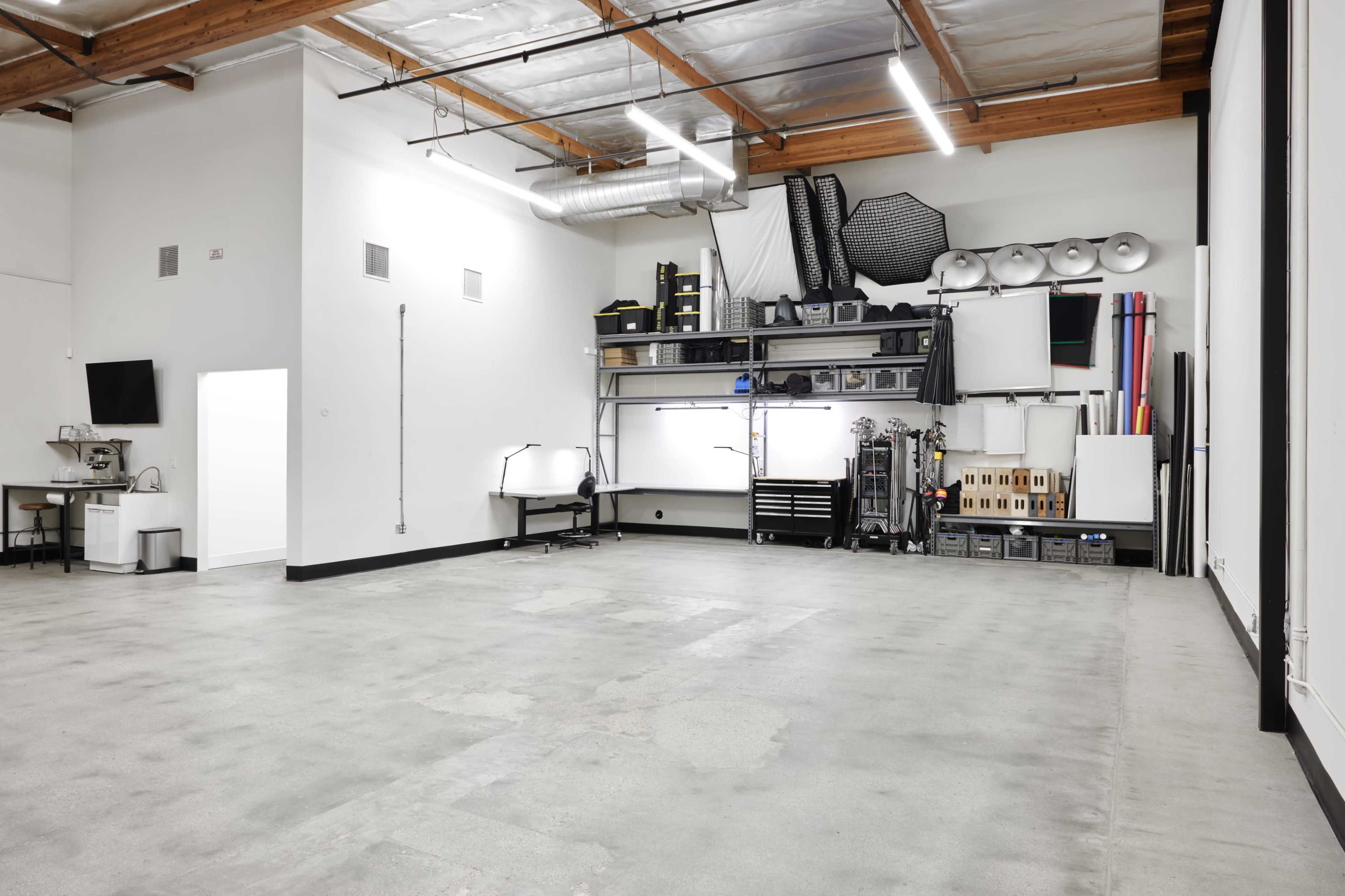 The image shows a spacious, empty garage or workshop with polished concrete flooring, unfinished walls, and organized shelves holding various tools and equipment.