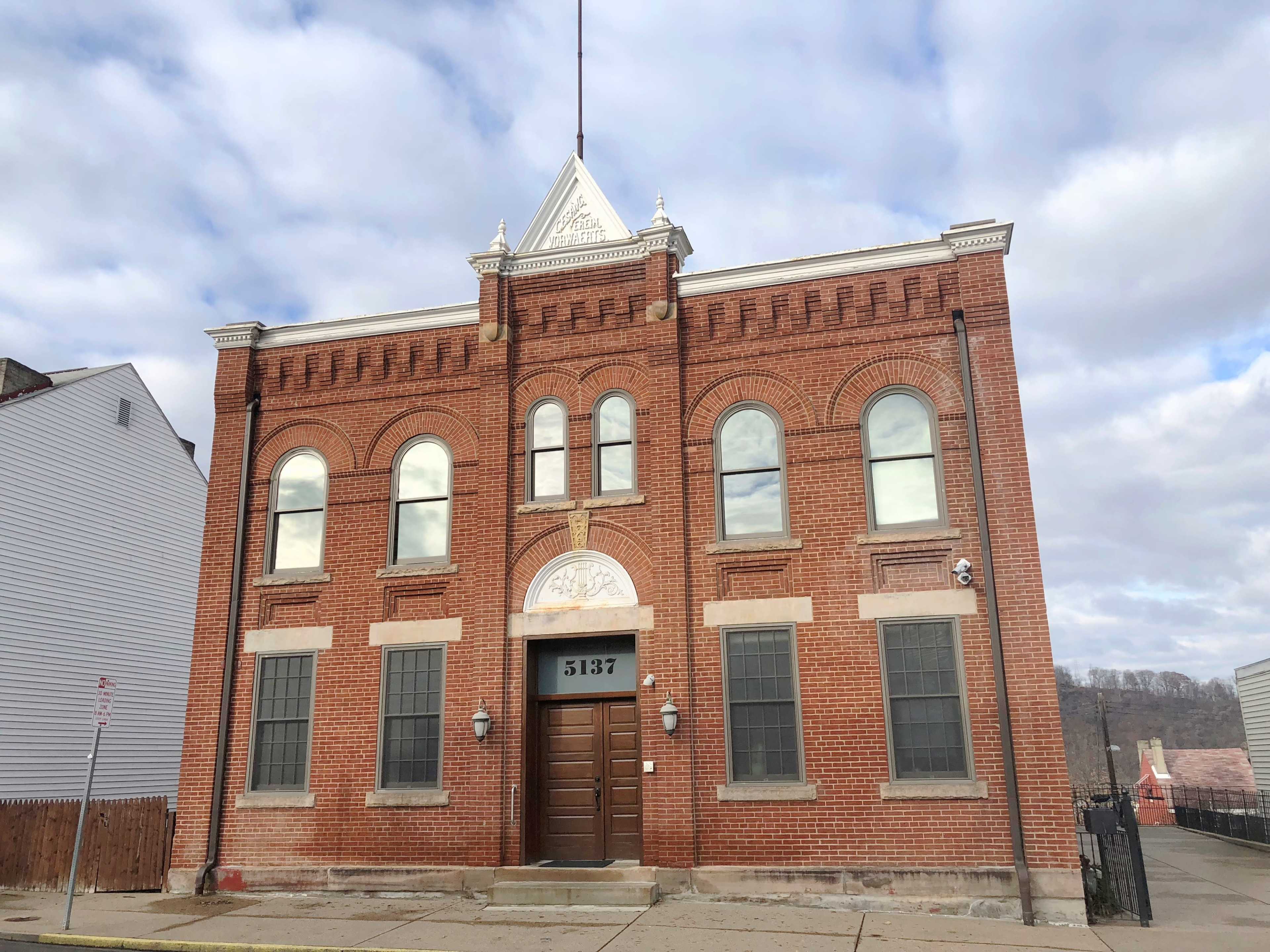 A brick building with arched windows and a central door, displaying the number 5137 above the entrance.