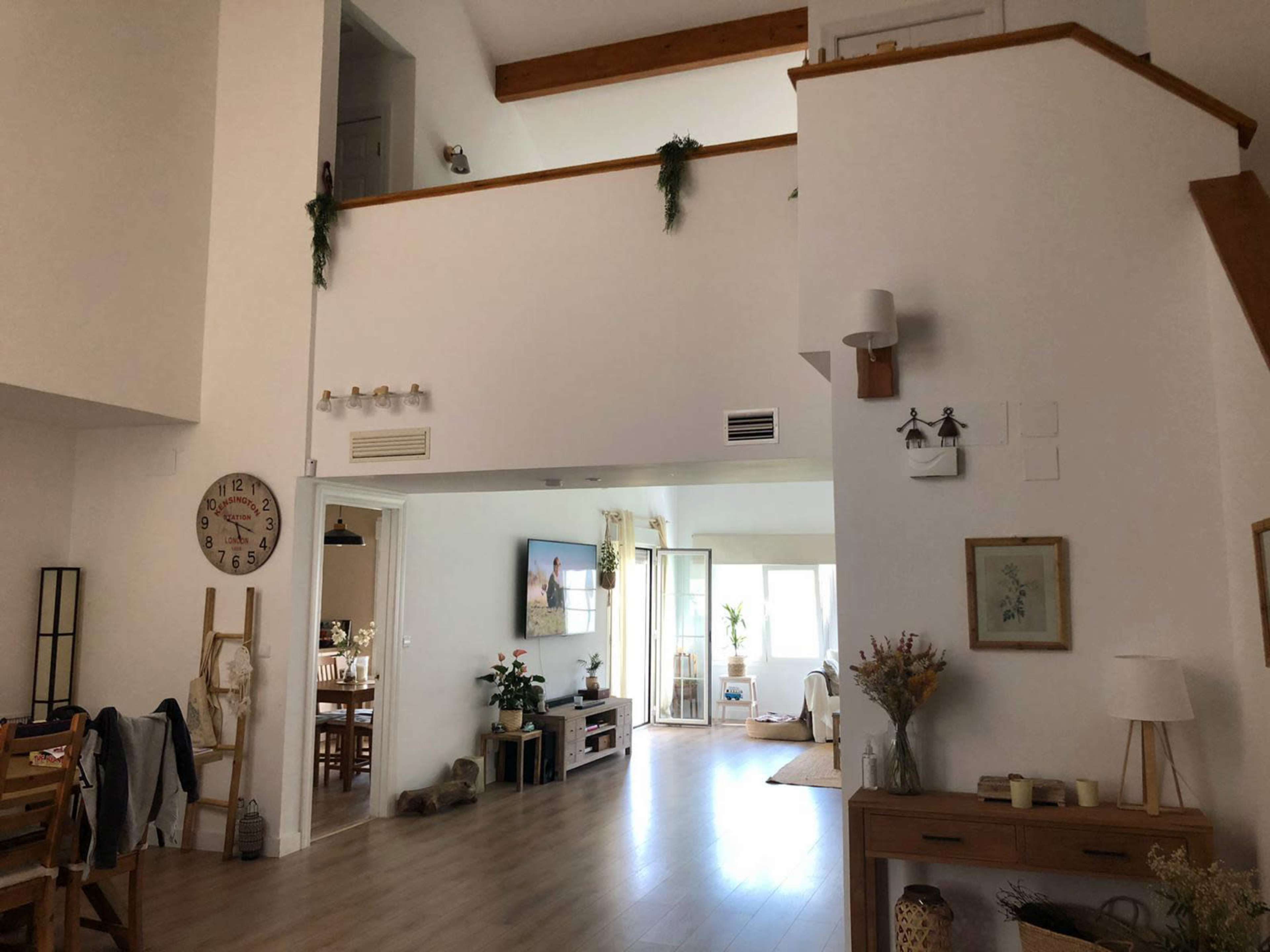 The image shows a spacious, open-concept living area with a staircase, large windows, and various decorative elements.