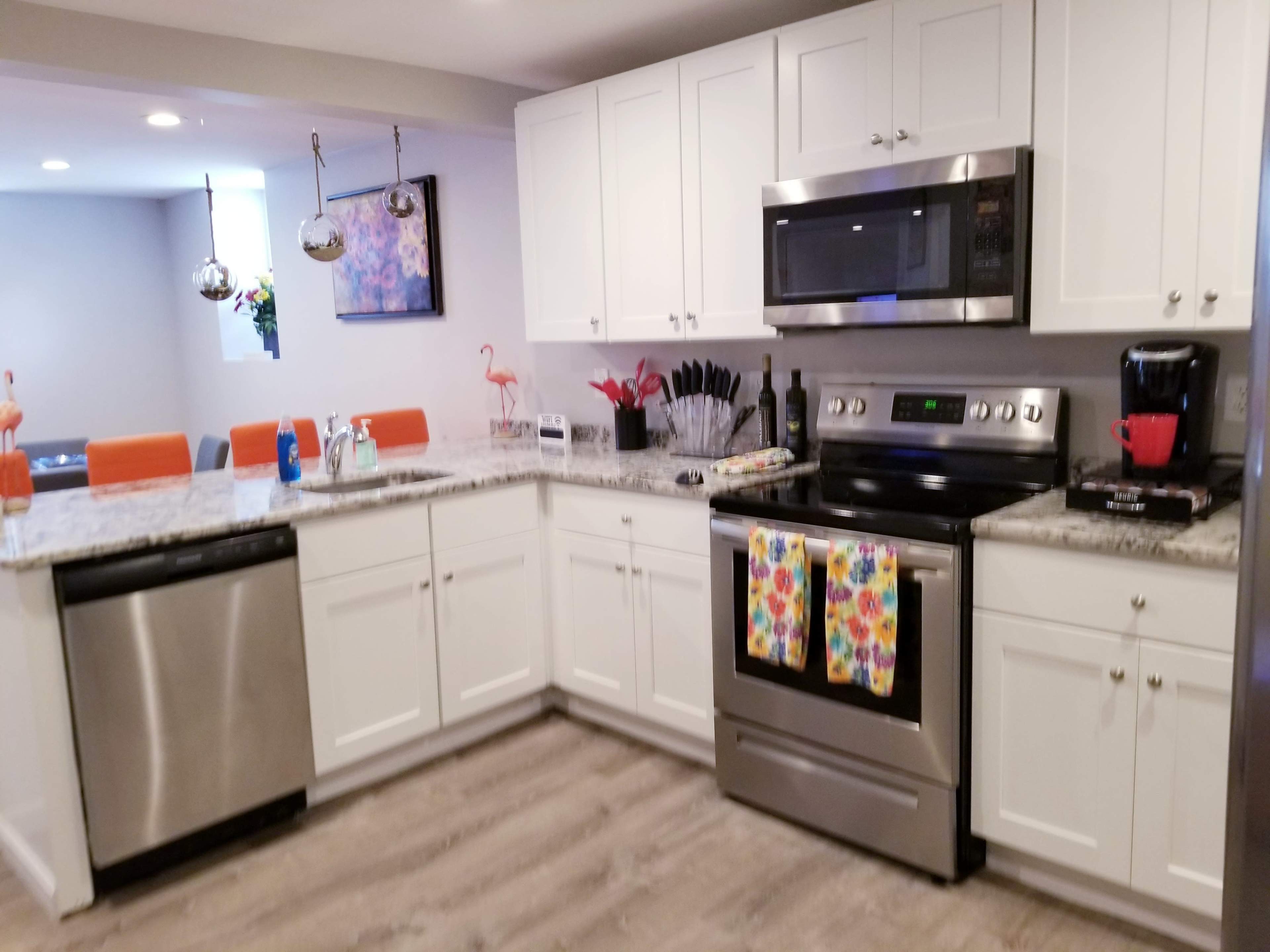 A modern kitchen with white cabinetry, stainless steel appliances, and a granite countertop, featuring colorful dish towels and decor elements.