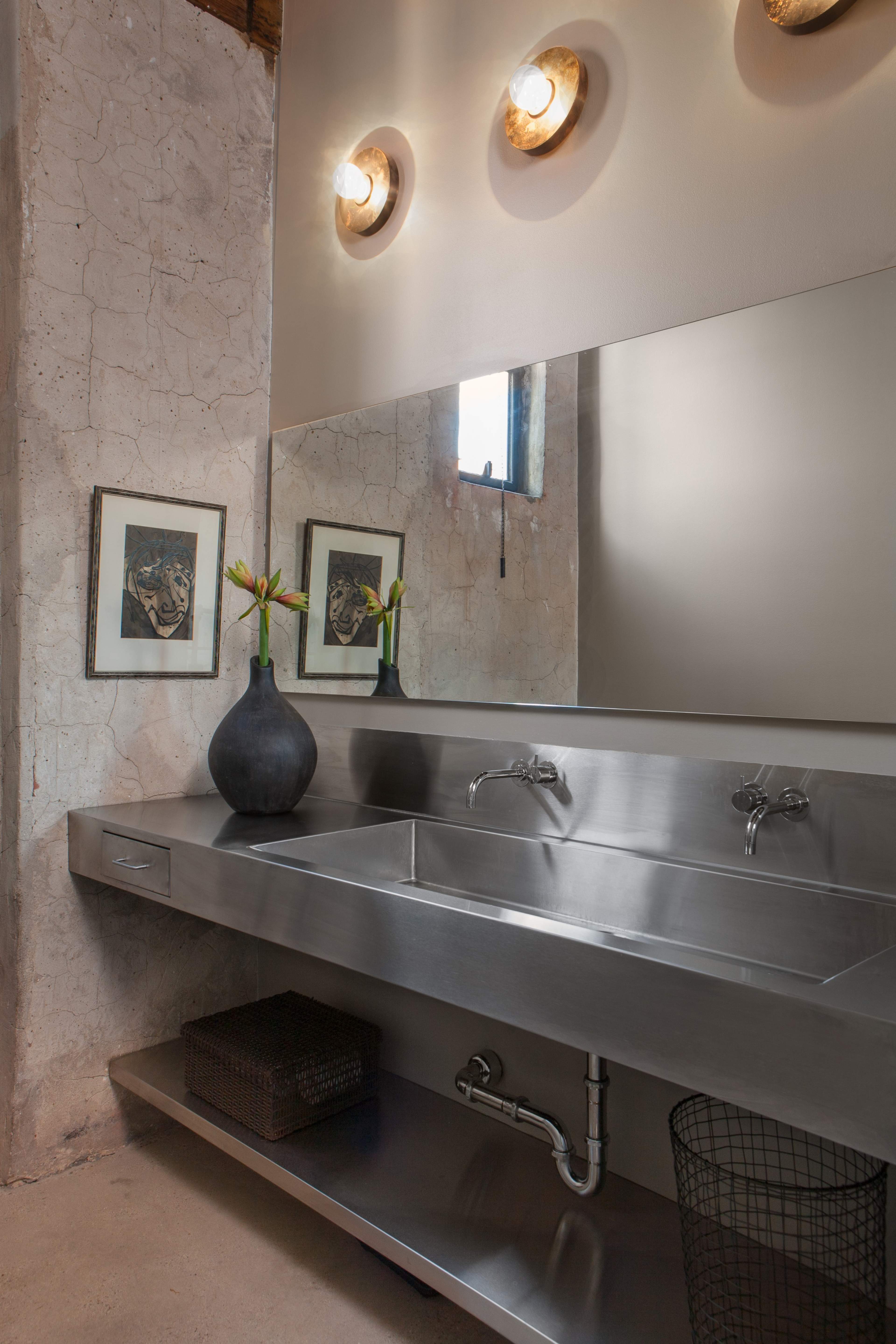 A modern bathroom featuring a stainless steel sink with dual faucets, framed artwork on the walls, and a vase with flowers on the countertop.