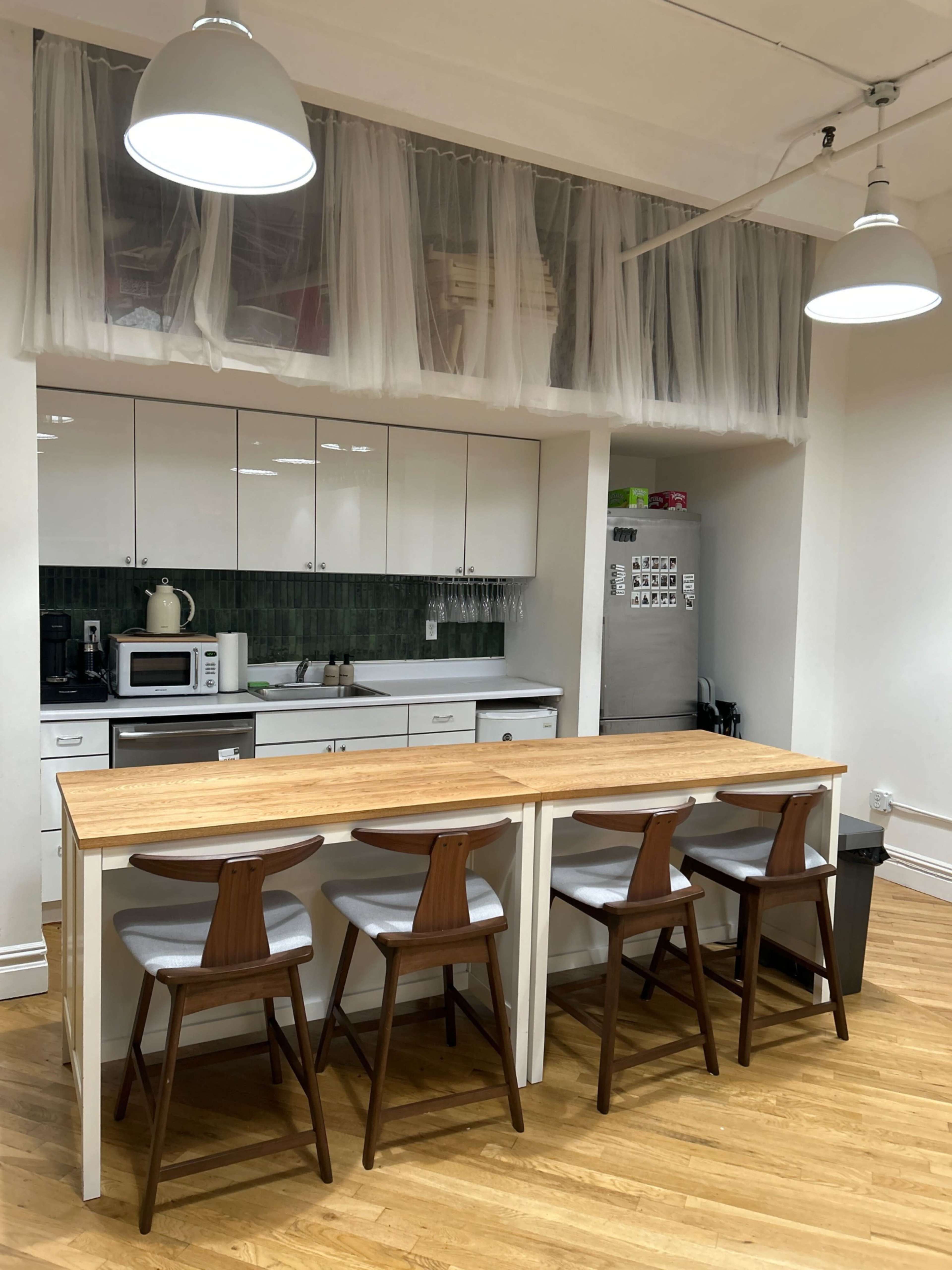 The image shows a modern kitchen with white cabinets, a wooden table, and four gray chairs, illuminated by hanging lights.