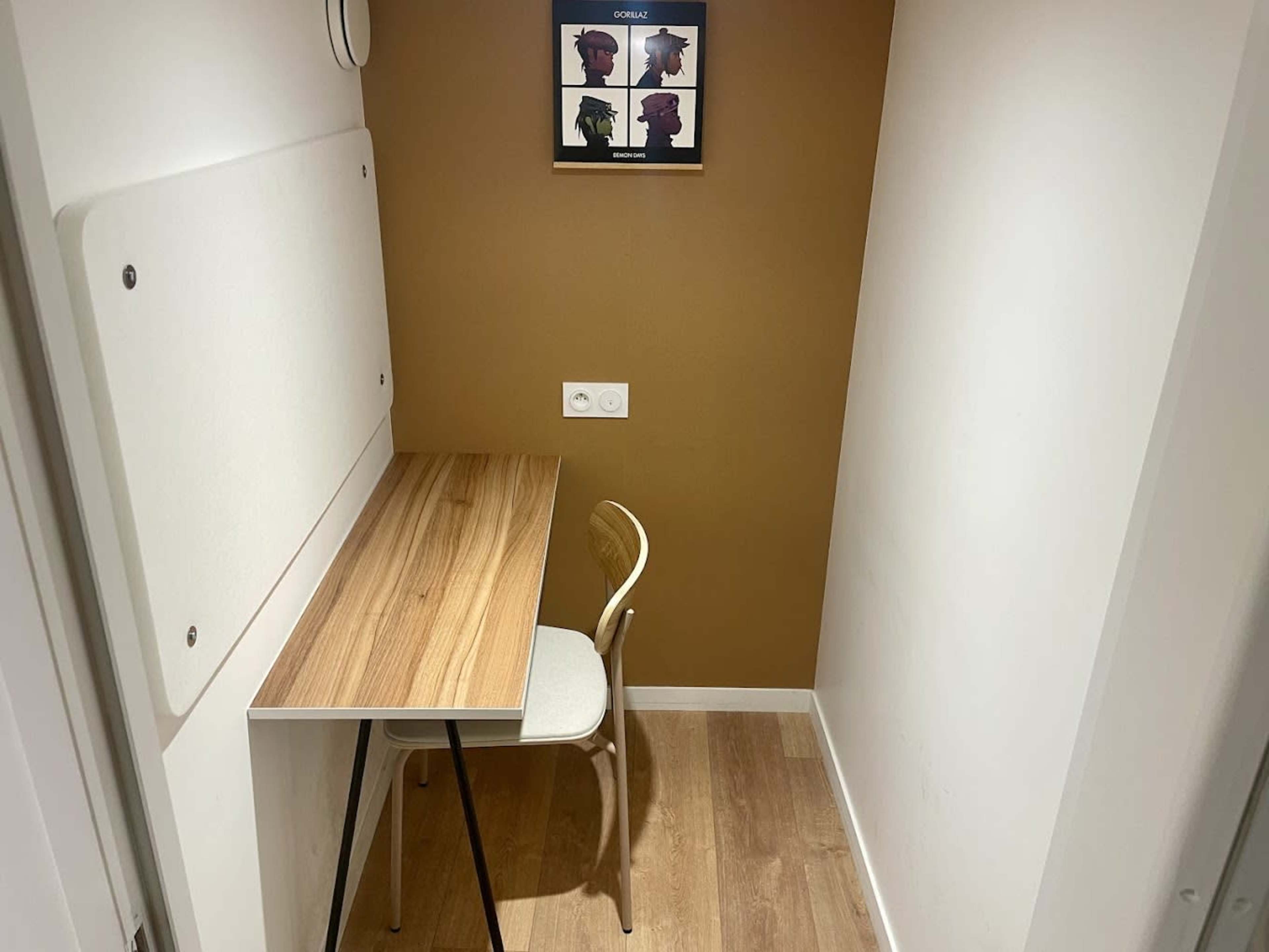 The image shows a small study nook with a wooden table and a single chair against a brown wall, featuring a framed artwork above the table.