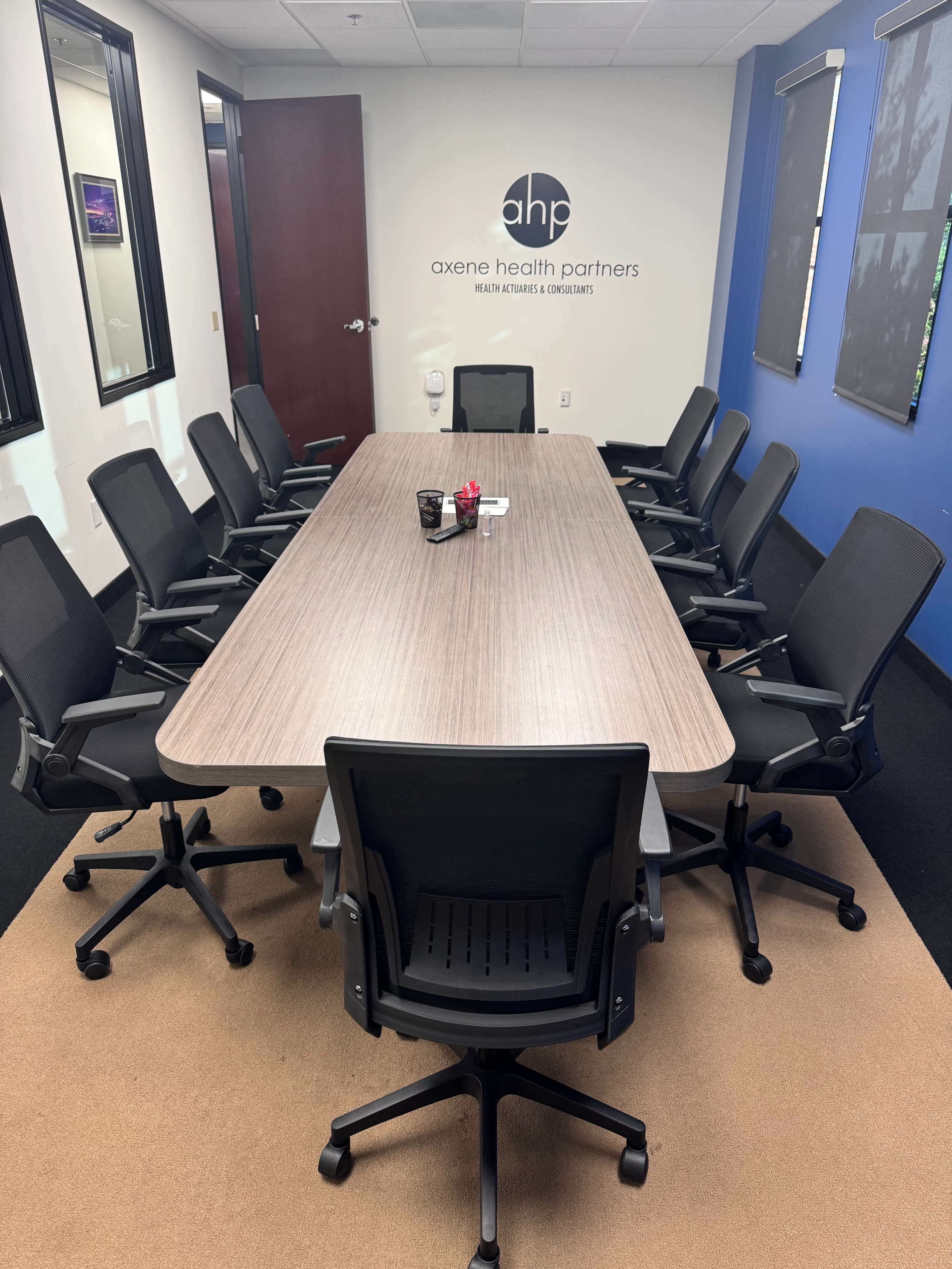A large conference room features a long wooden table surrounded by black office chairs, with a wall displaying the logo of Axene Health Partners.