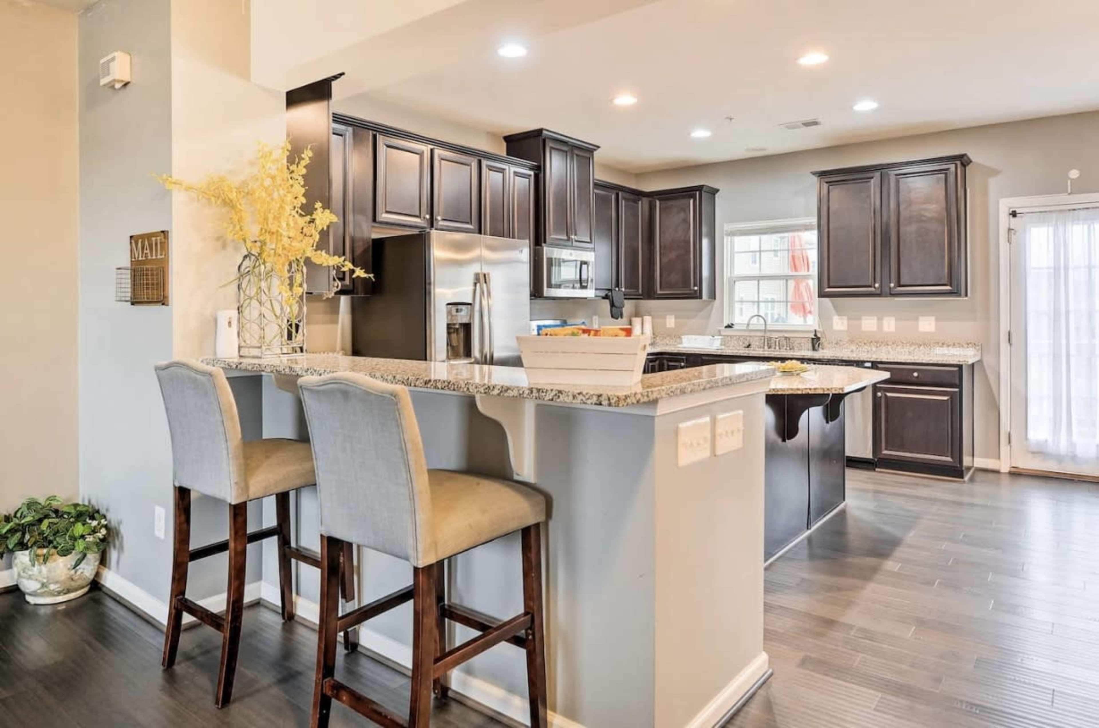A kitchen features dark wooden cabinets, granite countertops, and bar seating with stools.