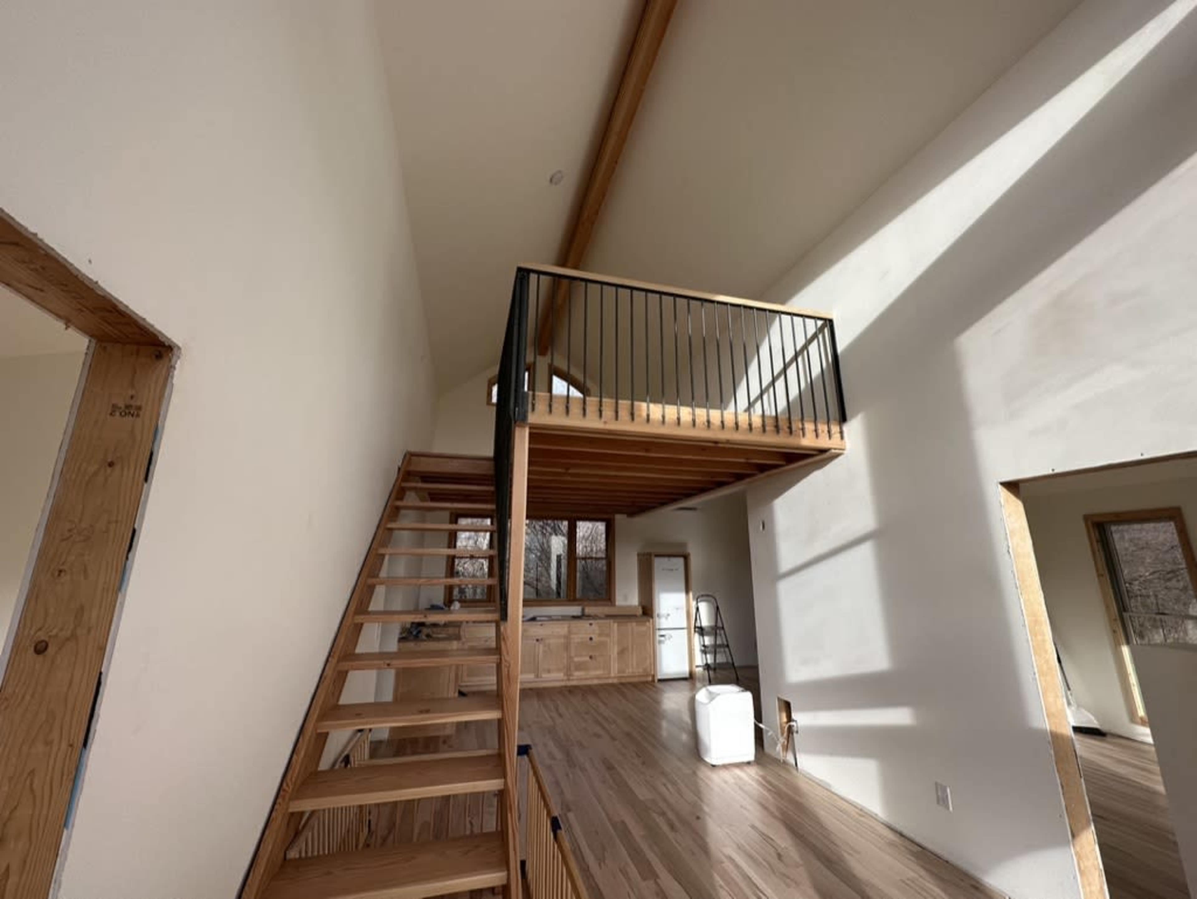 The image shows a bright, open interior of a house featuring a wooden staircase and a loft area with a railing.
