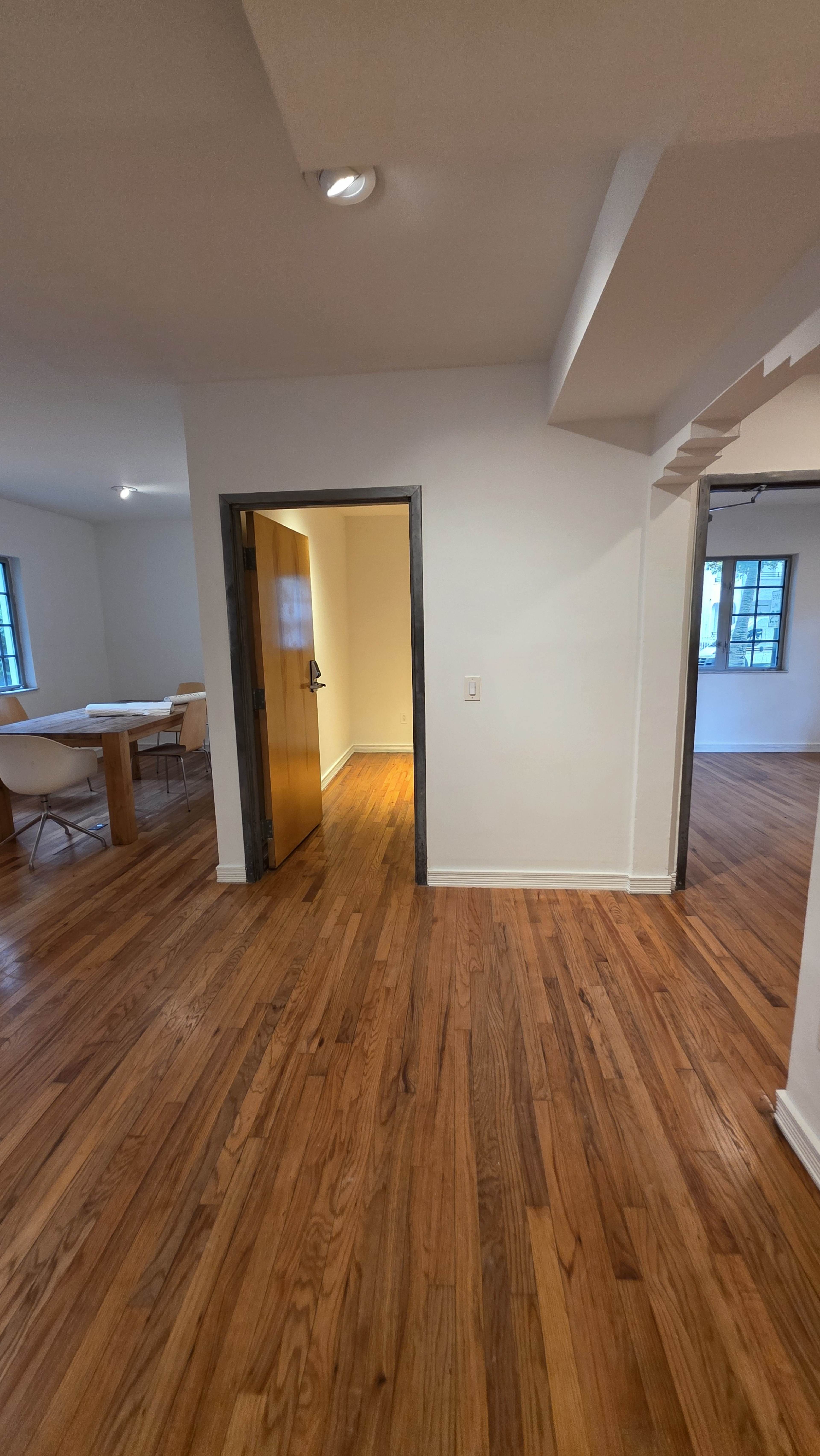 The image shows a hallway with hardwood floors leading to an open doorway, with adjacent rooms visible on either side.