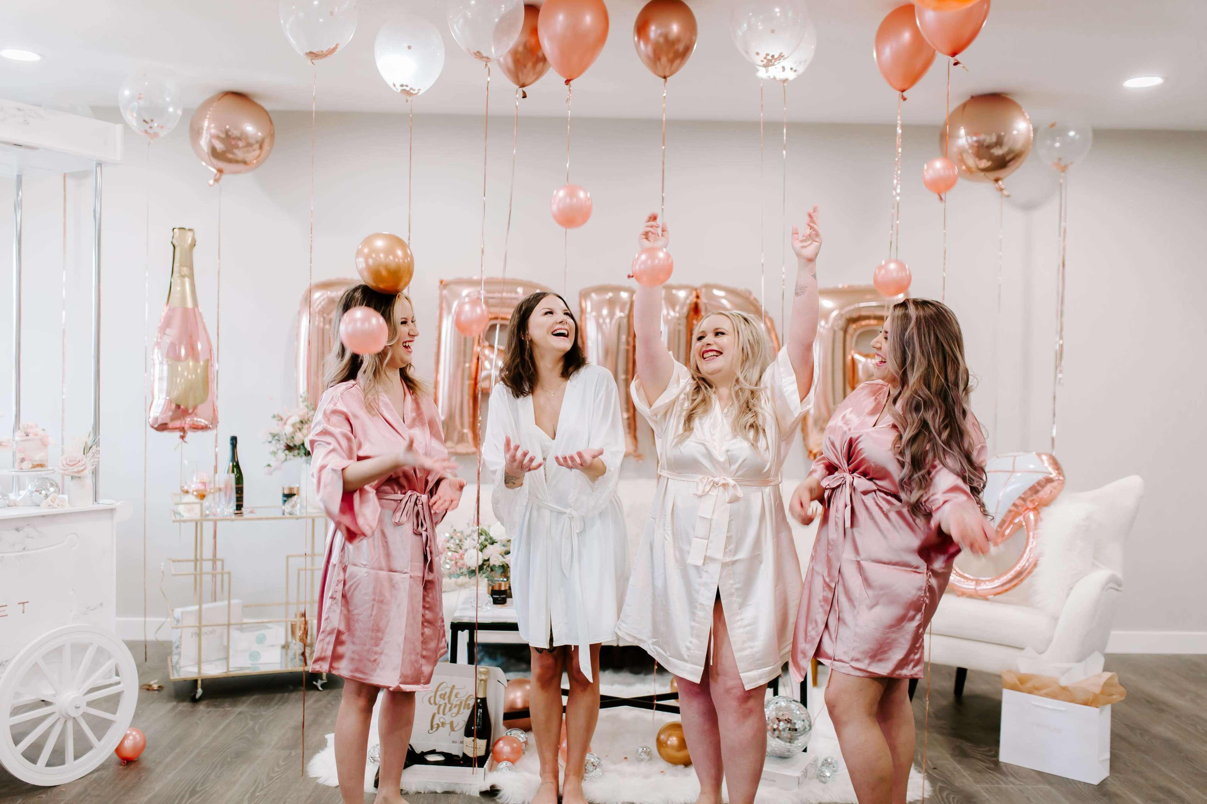 Four women in robes celebrate with balloons in a decorated room.