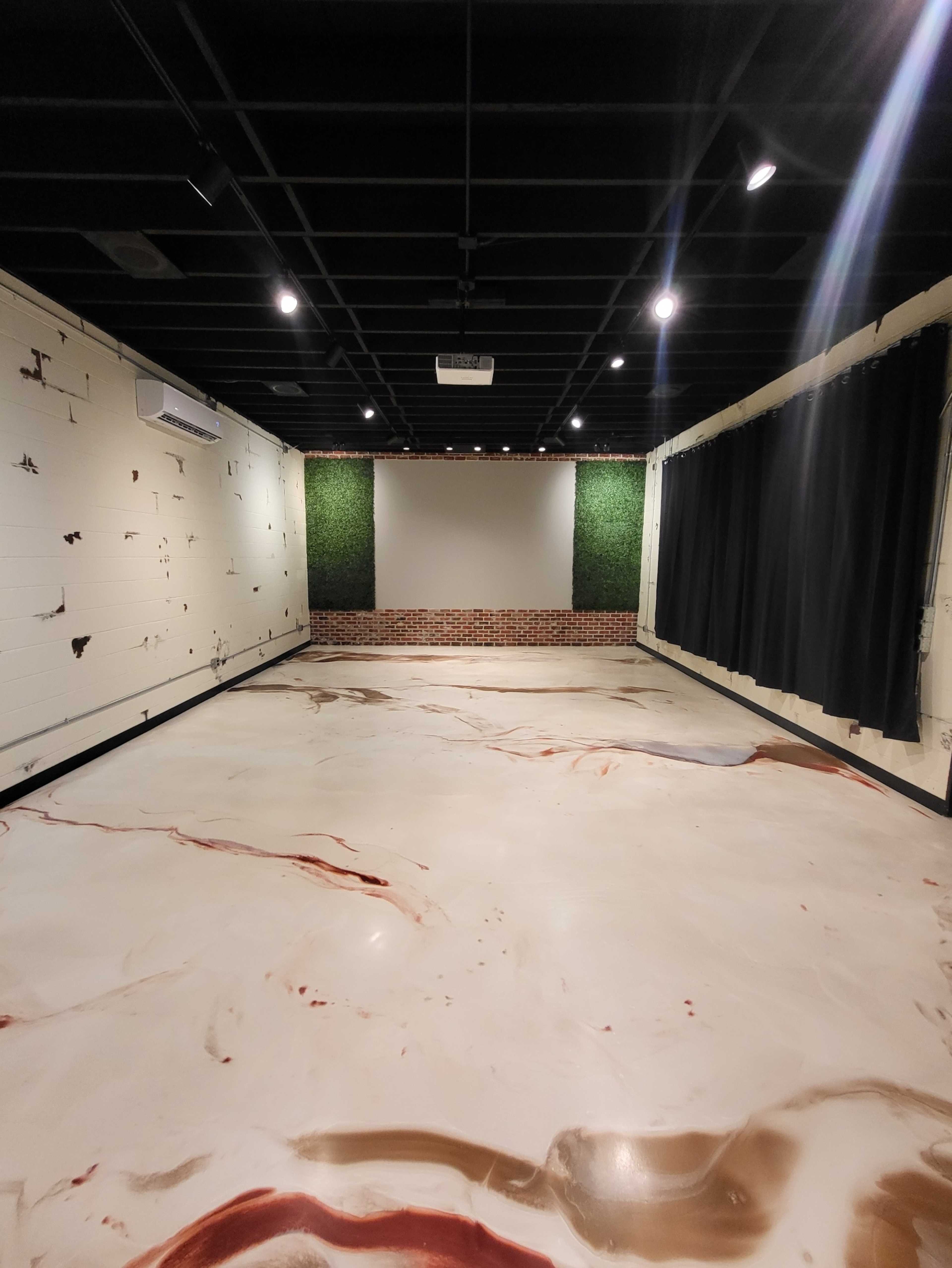 A spacious room with a marbled floor, a brick wall section, green wall decor, and black curtains.