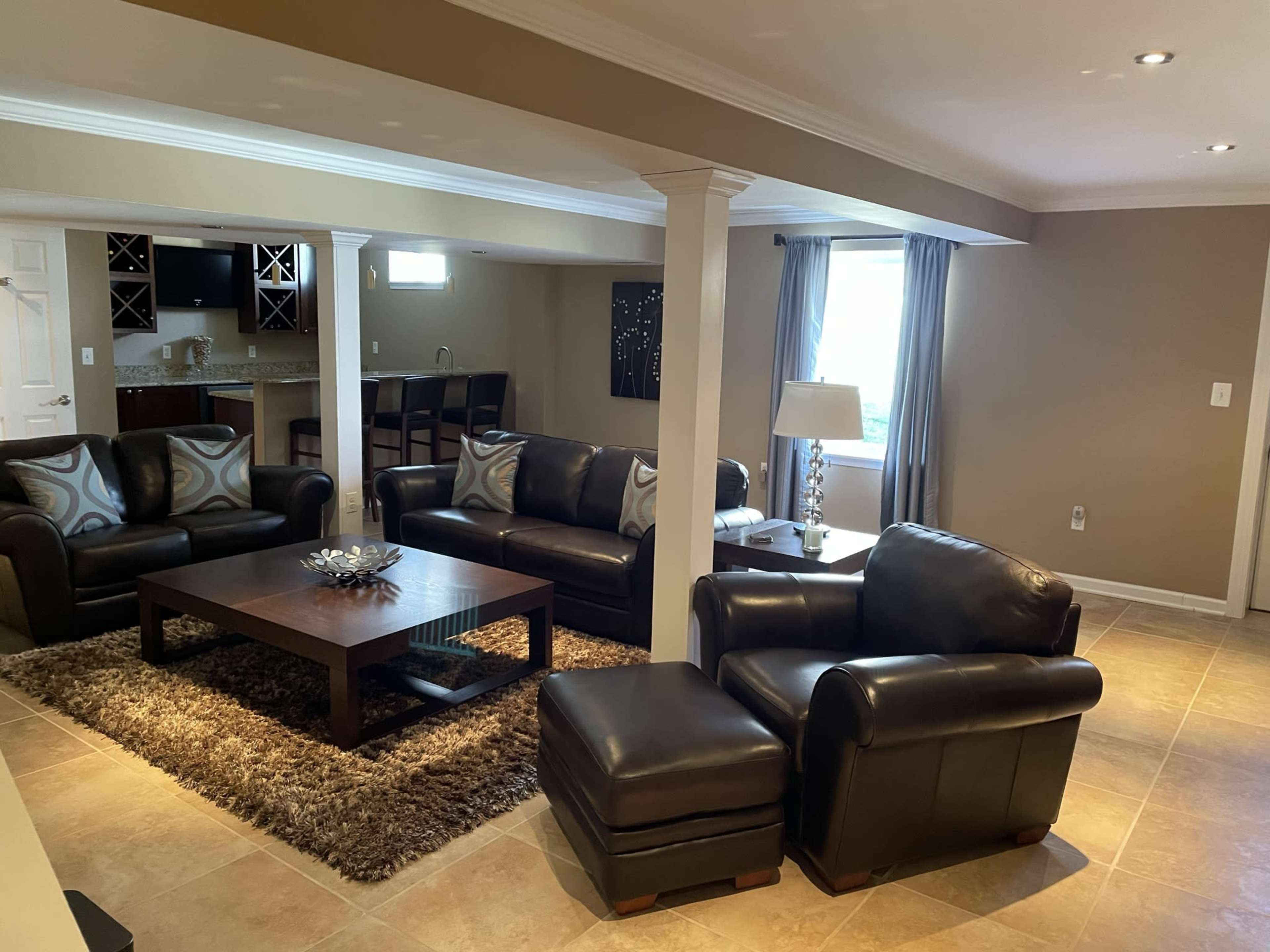 A modern, open-concept living area with dark leather sofas, a coffee table, and a dining area in the background.