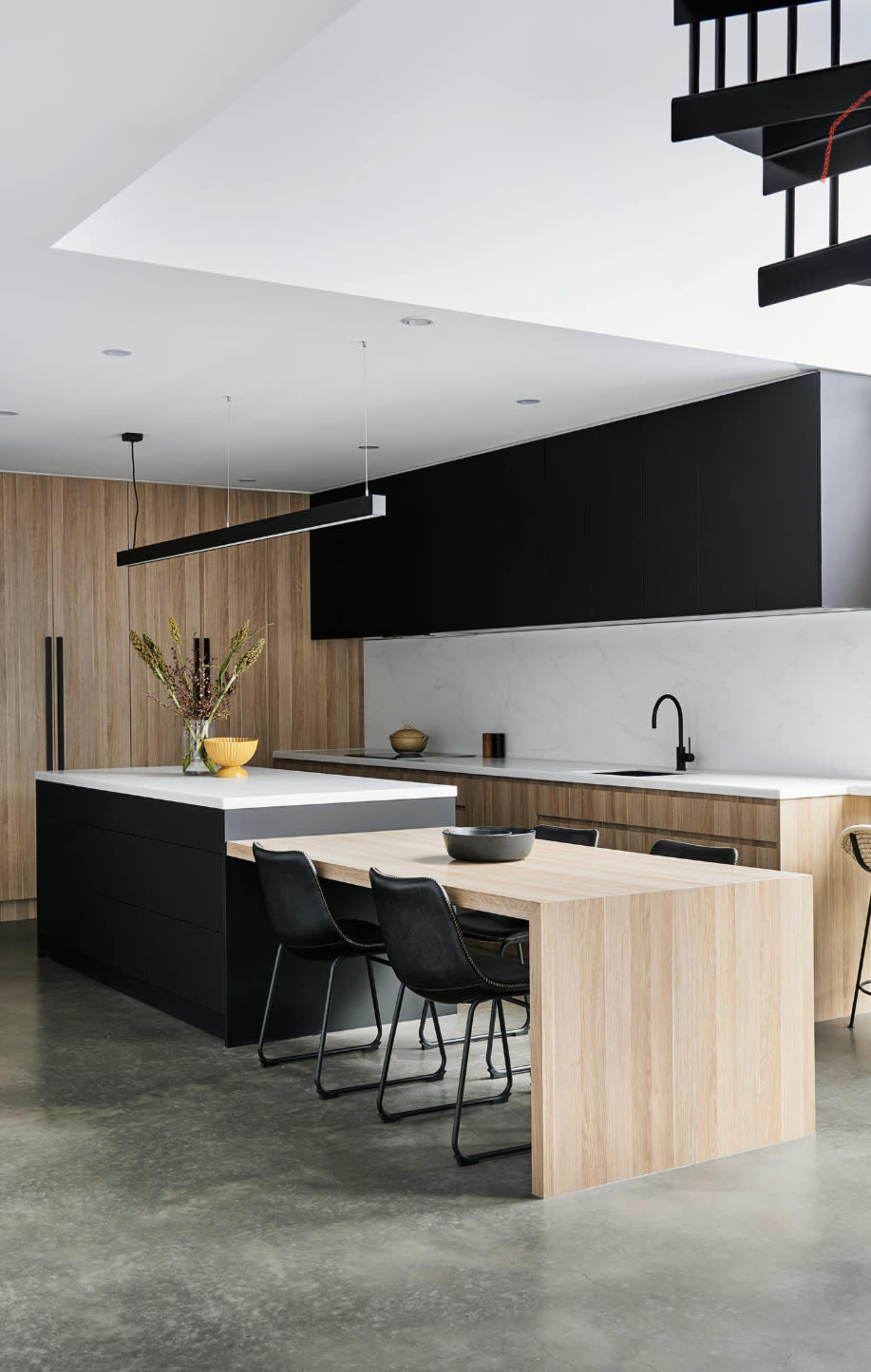 A modern kitchen features a sleek black and wood design with a central island and a dining area.