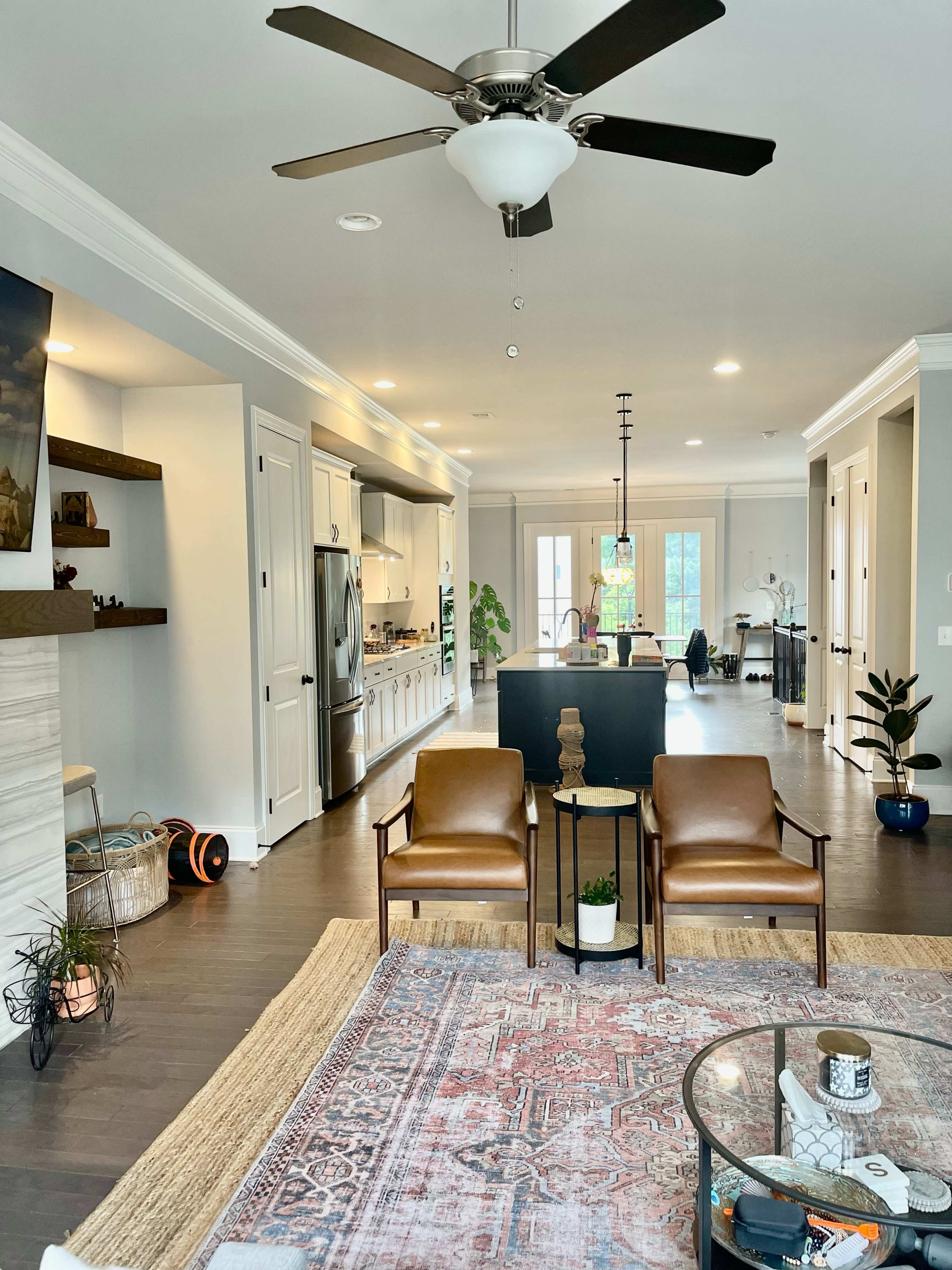 A modern open-concept living space features a seating area with two chairs, a coffee table, and a kitchen in the background.