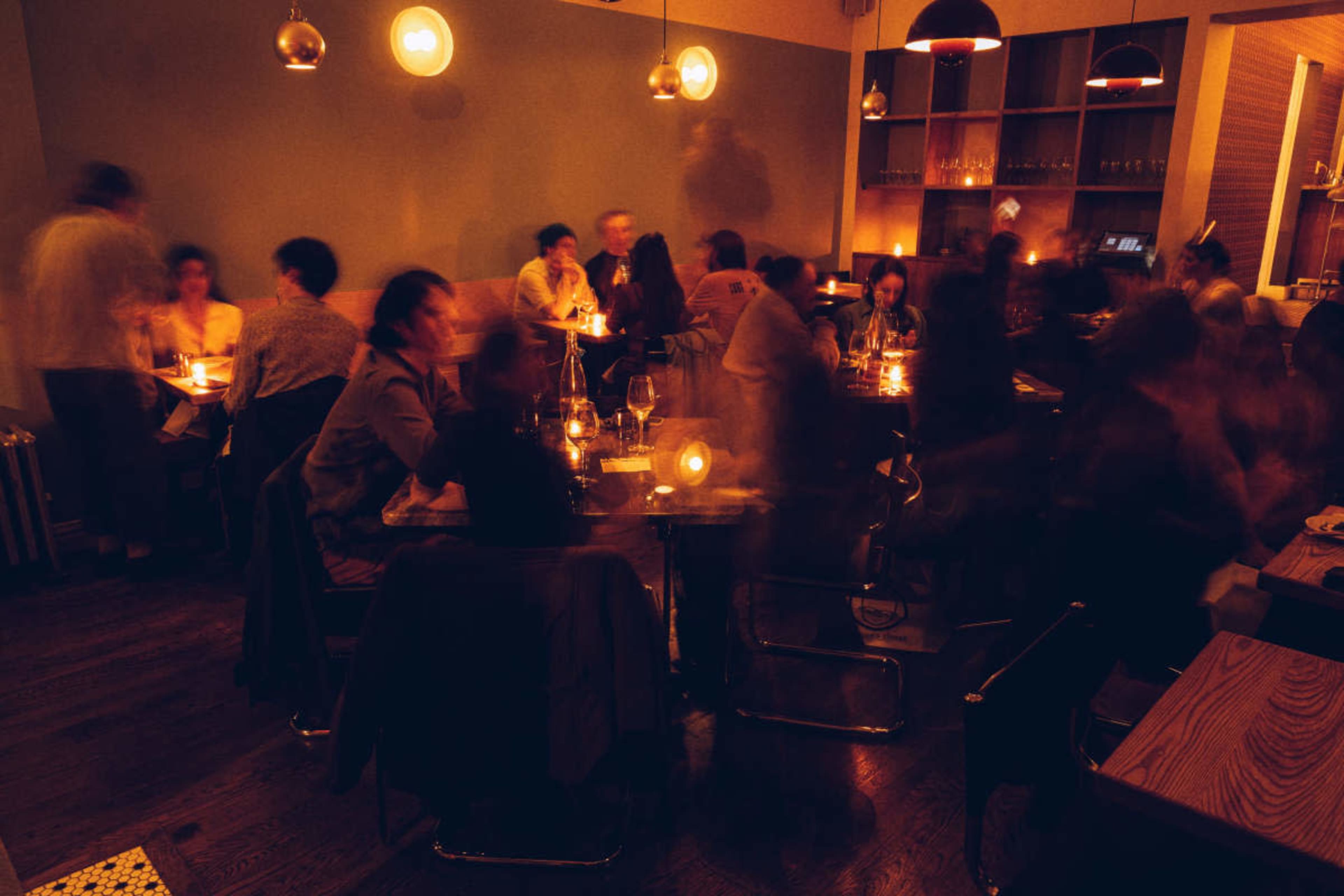 The image shows a dimly lit restaurant filled with people dining at tables, creating a lively atmosphere.