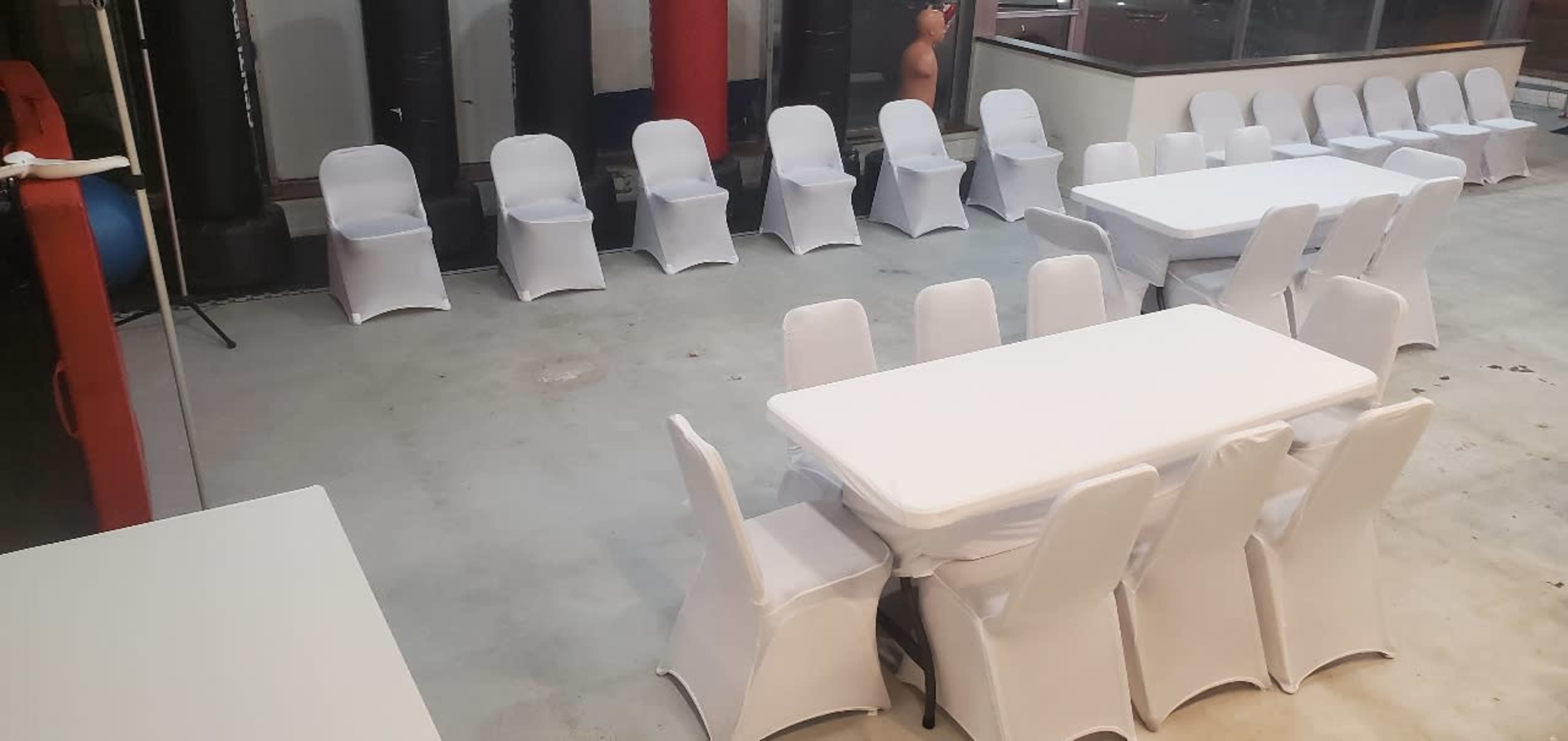A spacious indoor area is set up with numerous white tables and chairs, arranged in a circular pattern.