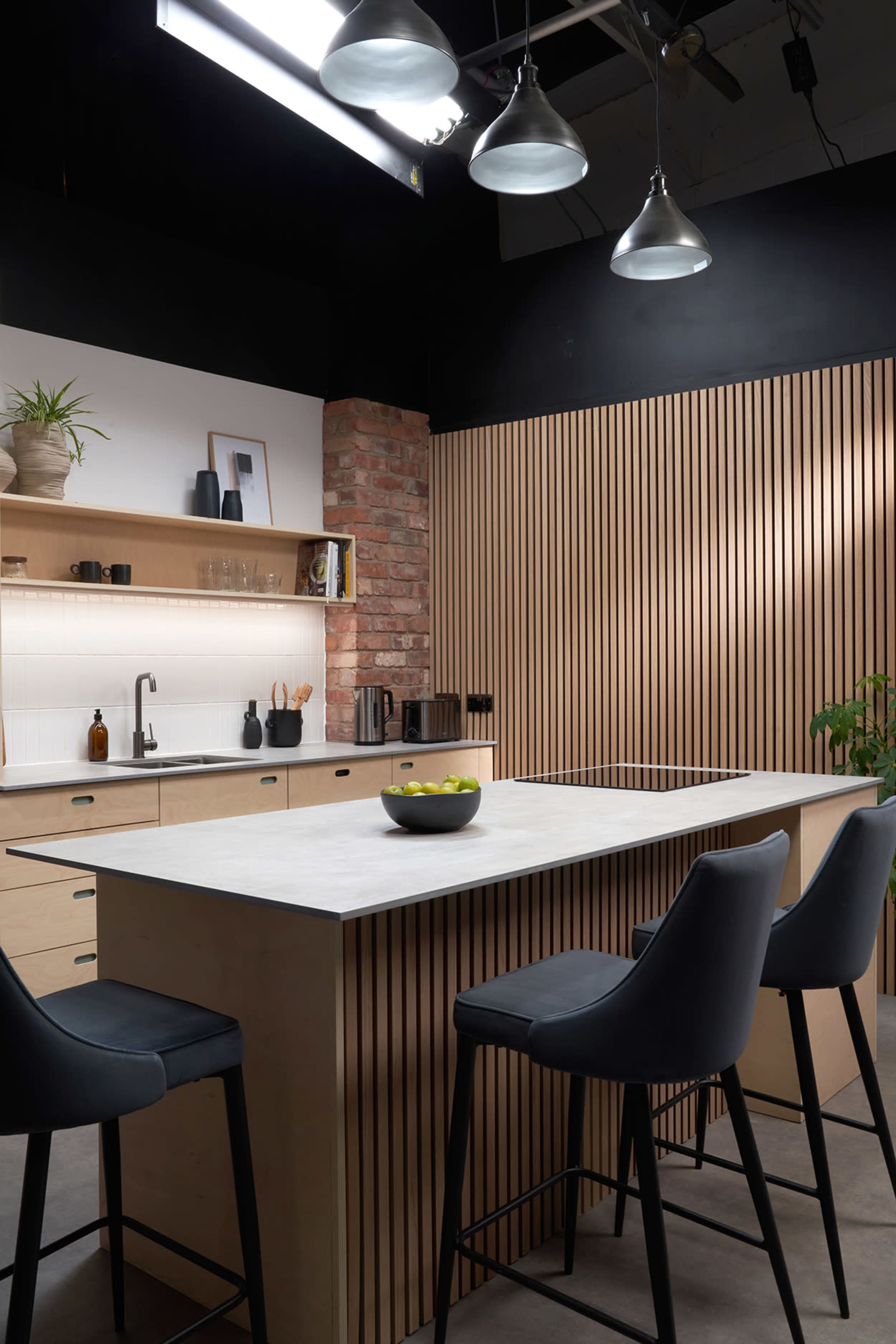 The modern kitchen features a central island with a bowl of fruit, surrounded by high stools, and is complemented by wooden paneling and pendant lighting.