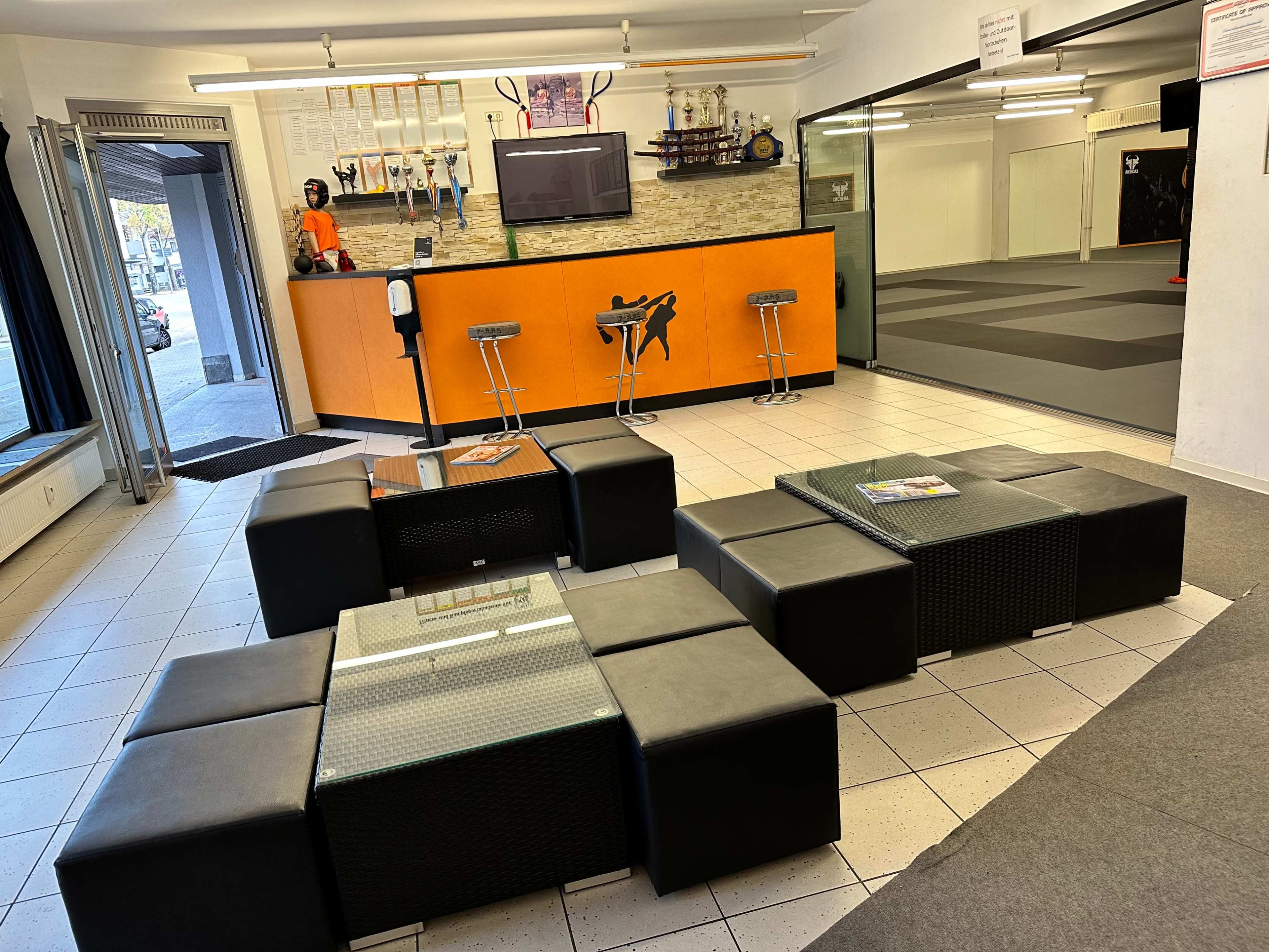 The image shows a modern reception area with black seating arrangements, a bar-style counter, and an open training space in the background.