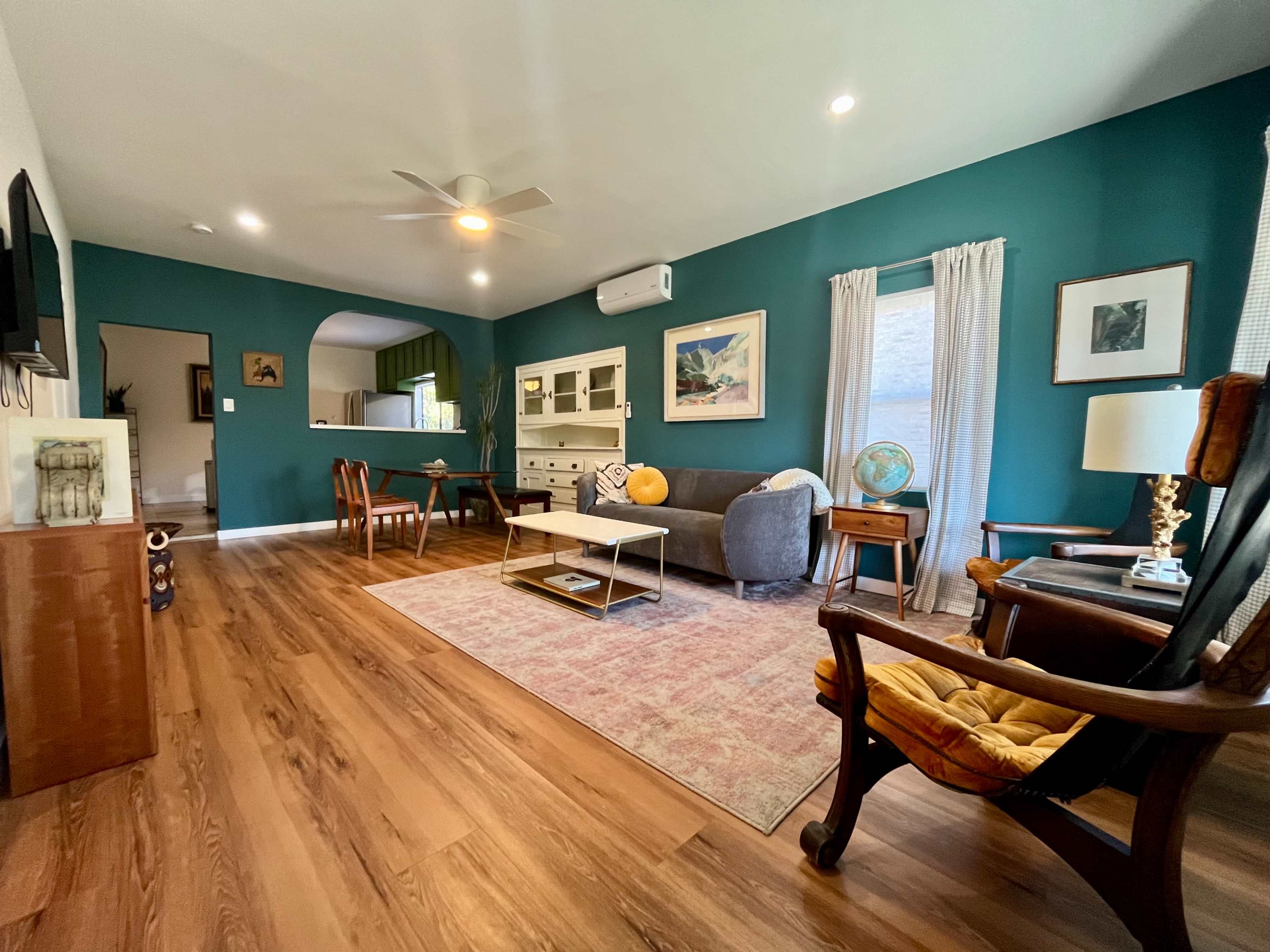 A modern living room featuring a teal accent wall, hardwood floors, and a mix of seating arrangements including a sofa and armchair.