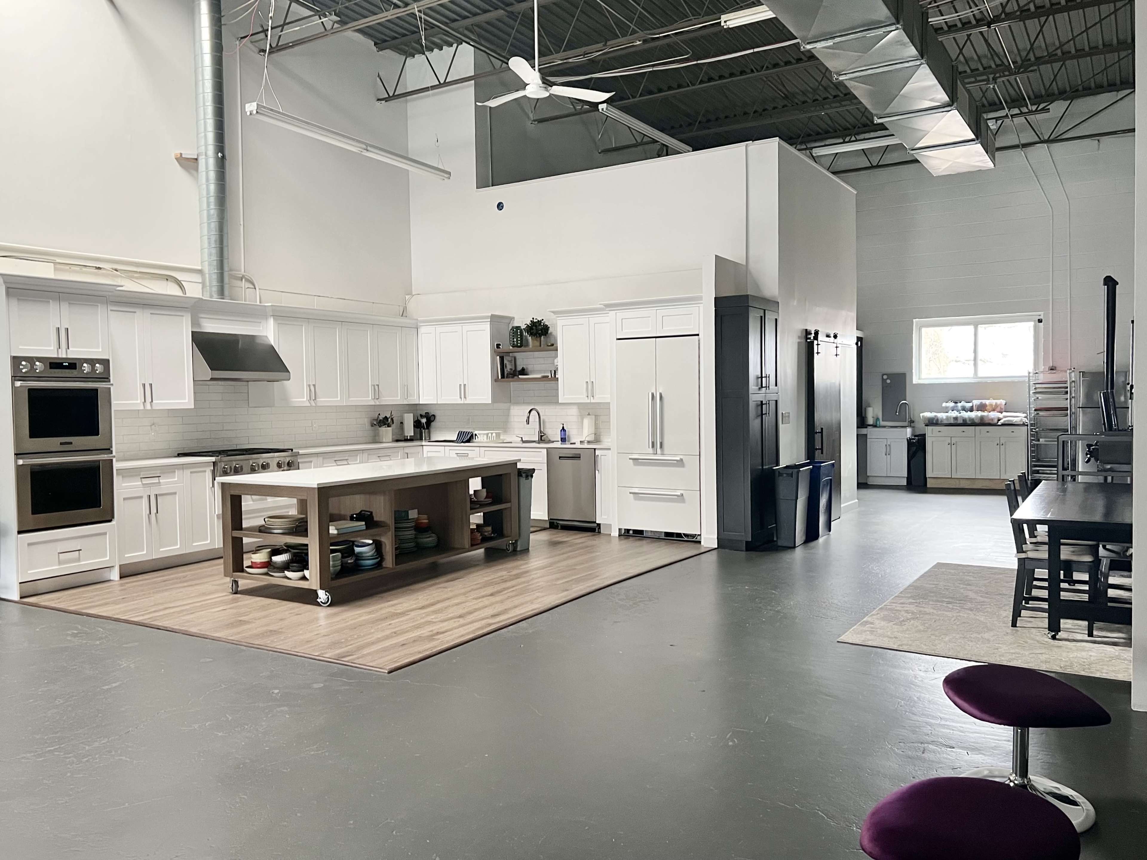 A spacious industrial kitchen with modern appliances, a central island, and a dining table set against a backdrop of white cabinetry and gray floors.