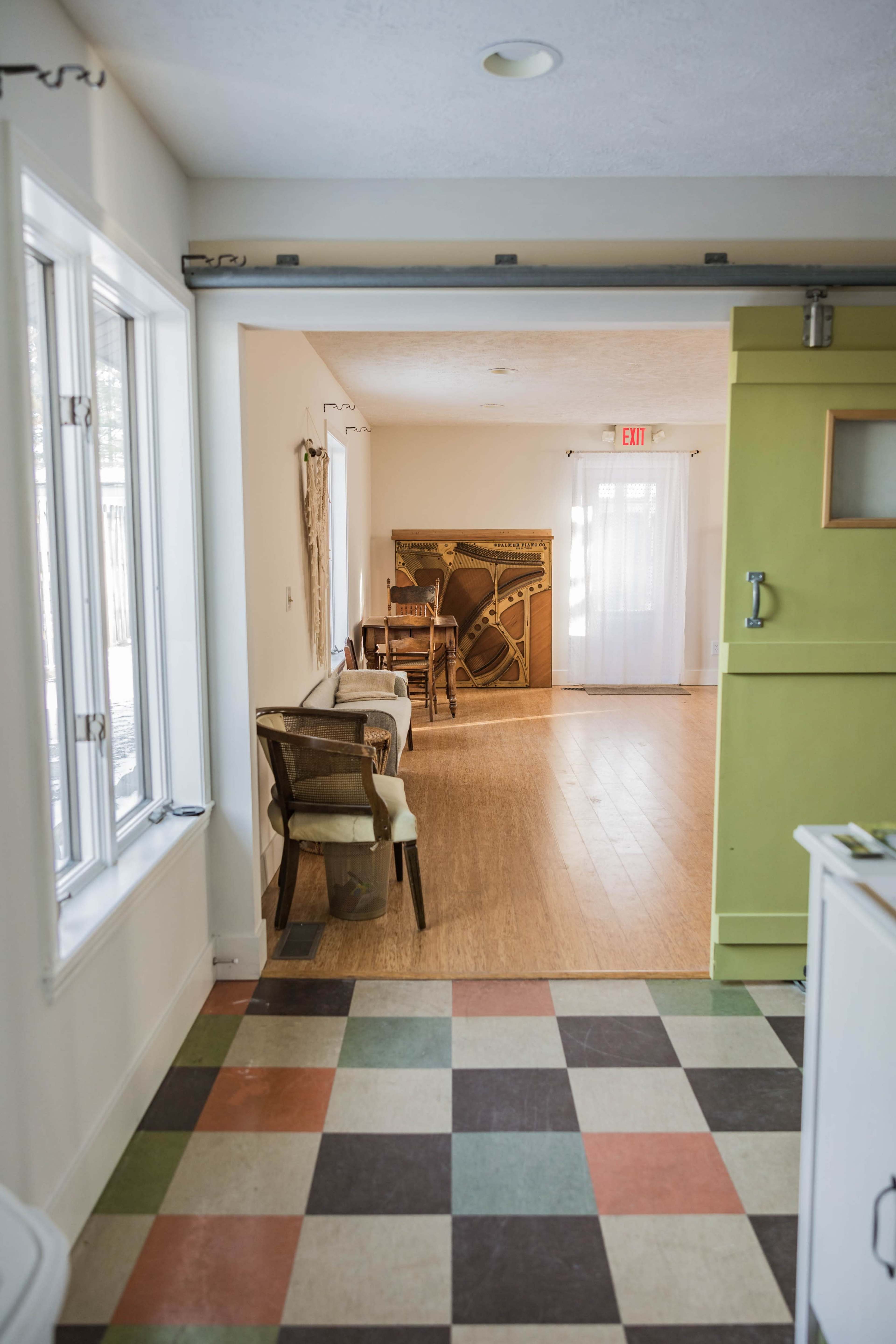 A view from a kitchen into a spacious room featuring a green refrigerator, chairs, and a decorative wall art.