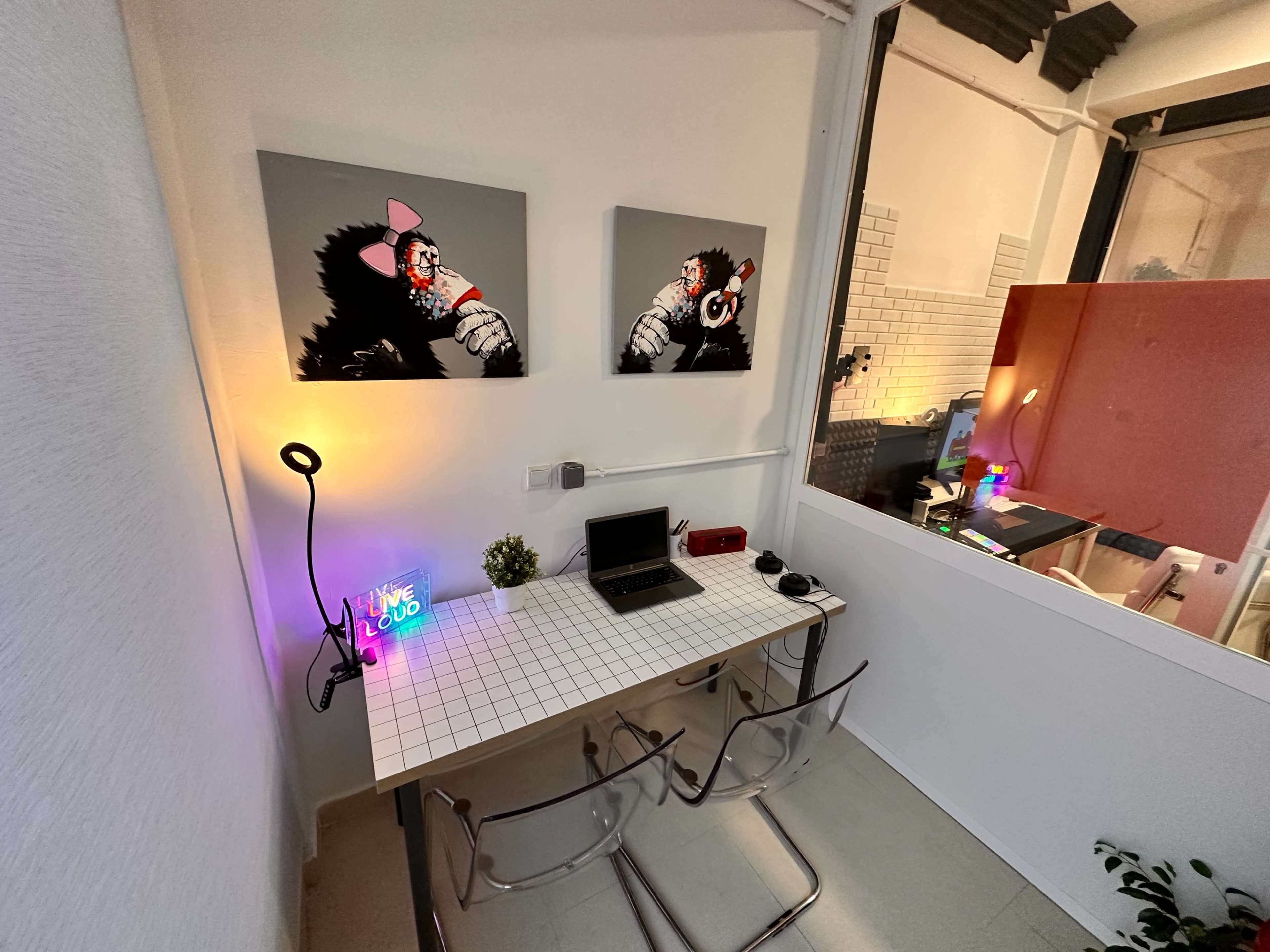 A small office space features a table with a laptop, vibrant artwork on the walls, and decorative lighting.